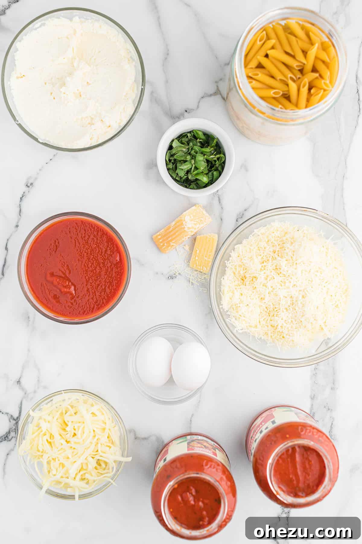 Effortless Slow Cooker Baked Ziti 3 An array of fresh ingredients including penne pasta, jarred sauces, ricotta, basil, and cheeses, laid out for preparing baked ziti.