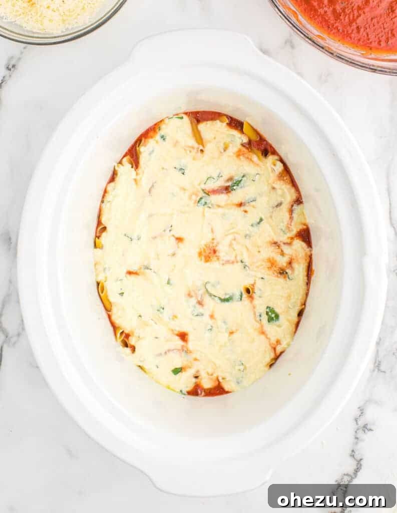 Effortless Slow Cooker Baked Ziti 9 The creamy ricotta mixture being evenly spread over the pasta layer in the slow cooker.