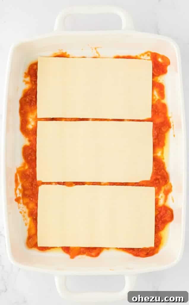 Triple Cheese Lasagna 11 Three lasagna noodles laid neatly over the first layer of sauce in a baking dish, forming the base for the cheese filling.