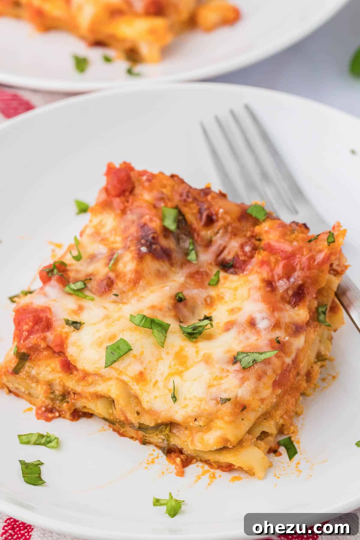 Triple Cheese Lasagna 26 A generous slice of cheese lasagna, topped with fresh basil, served on a white plate, ready to be enjoyed.