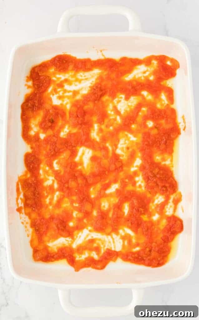 Triple Cheese Lasagna 10 A thin layer of pasta sauce evenly spread across the bottom of a 9x13 inch baking dish, ready for the first layer of noodles.