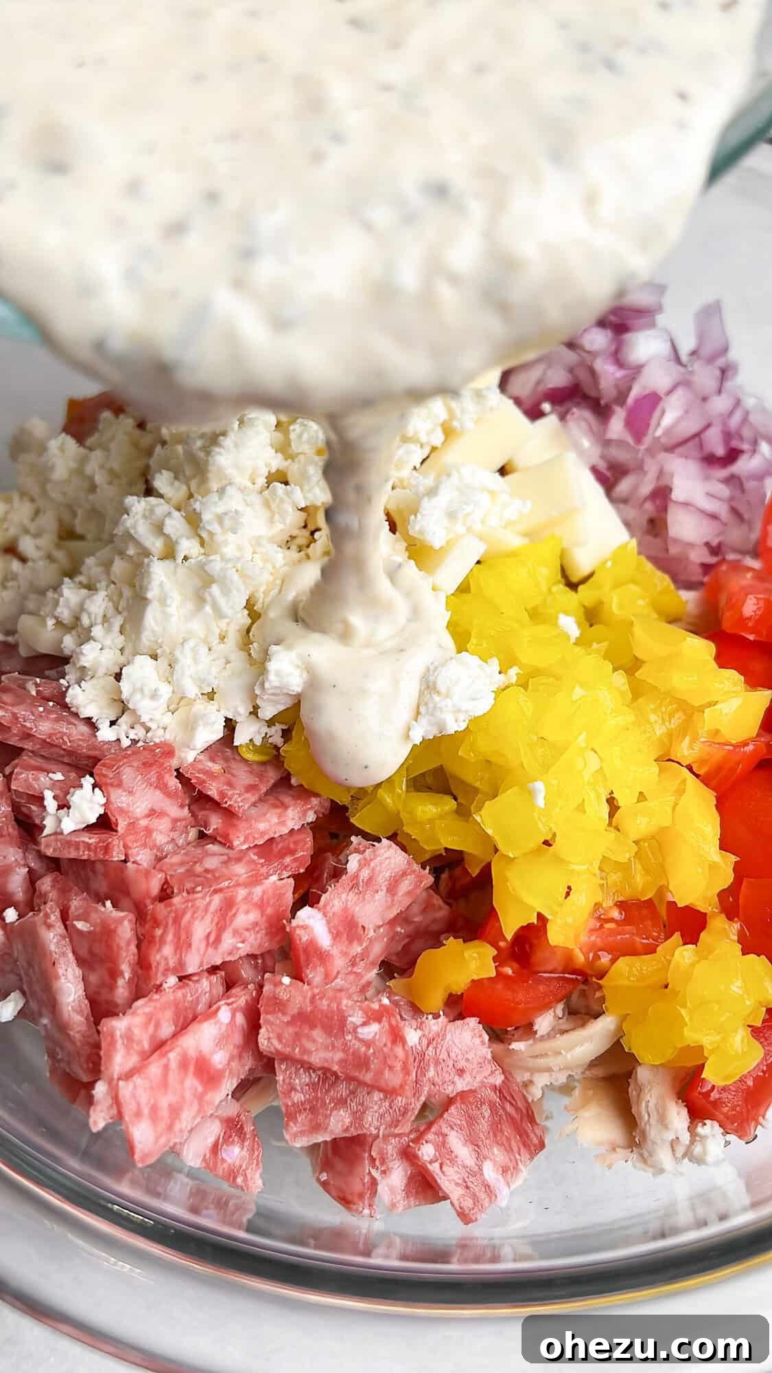 Someone drizzling the creamy grinder dressing over the assembled chicken salad ingredients in a bowl.