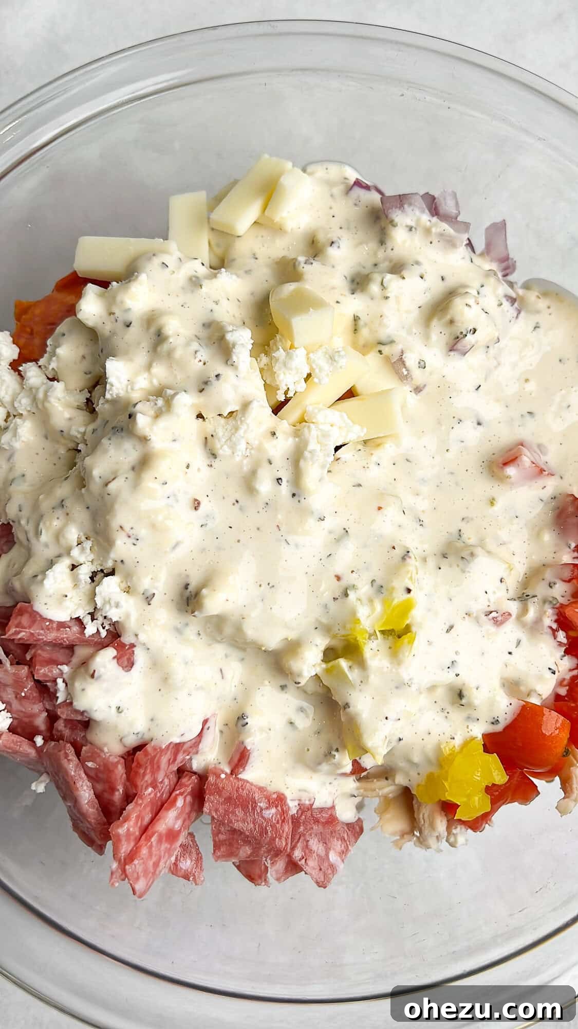 The Italian Grinder Chicken Salad in a bowl, with the dressing freshly poured over and ready to be tossed.