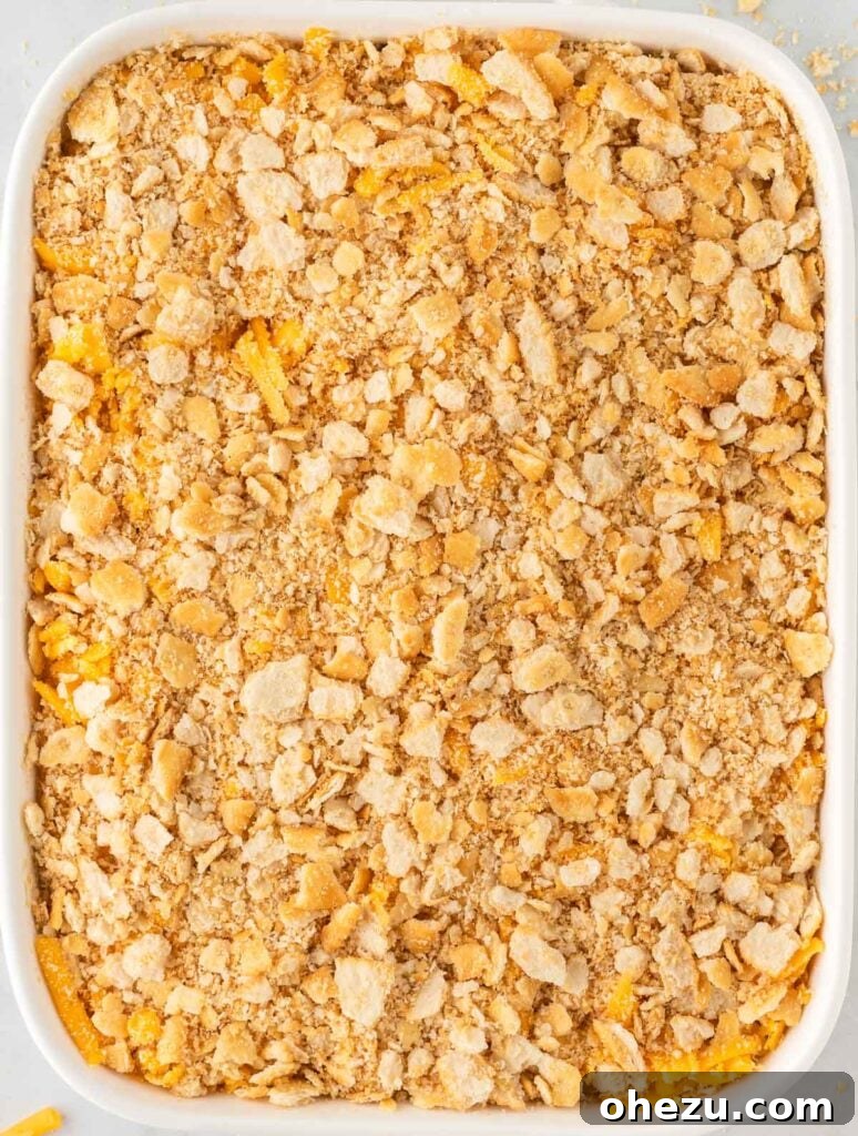 Broccoli casserole topped with cheddar cheese and crushed Ritz crackers, ready for baking