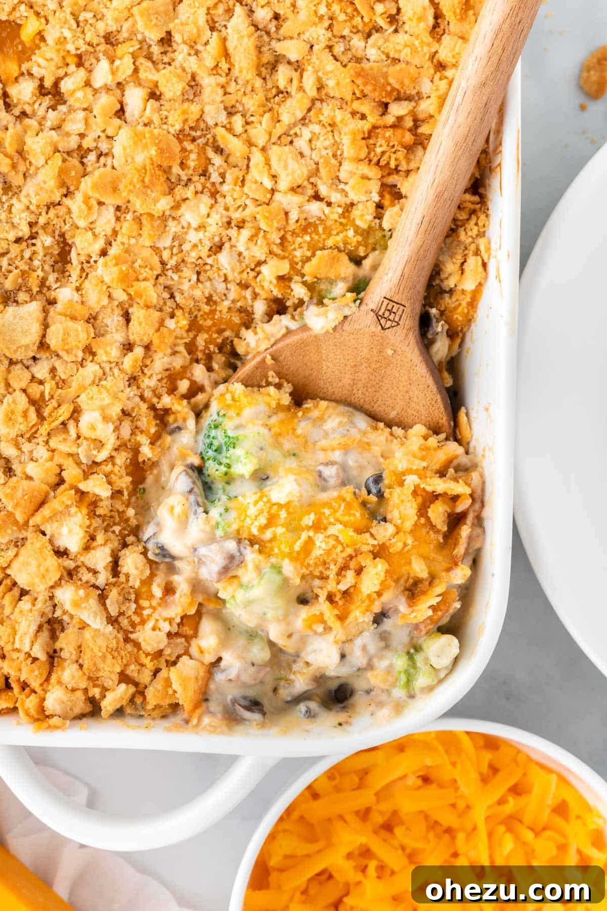 Wooden scoop taking a generous portion of cheesy Ritz broccoli casserole from the dish