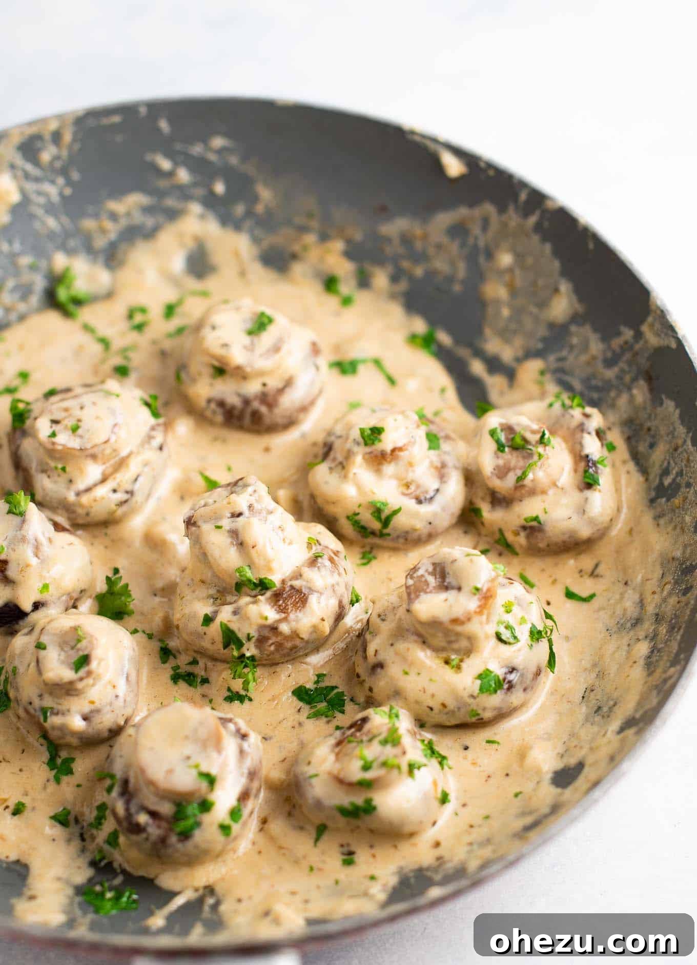 Sautéed portobello mushrooms smothered in a rich, creamy garlic Parmesan sauce, elegantly garnished with fresh parsley in a cast-iron skillet, ready to serve.