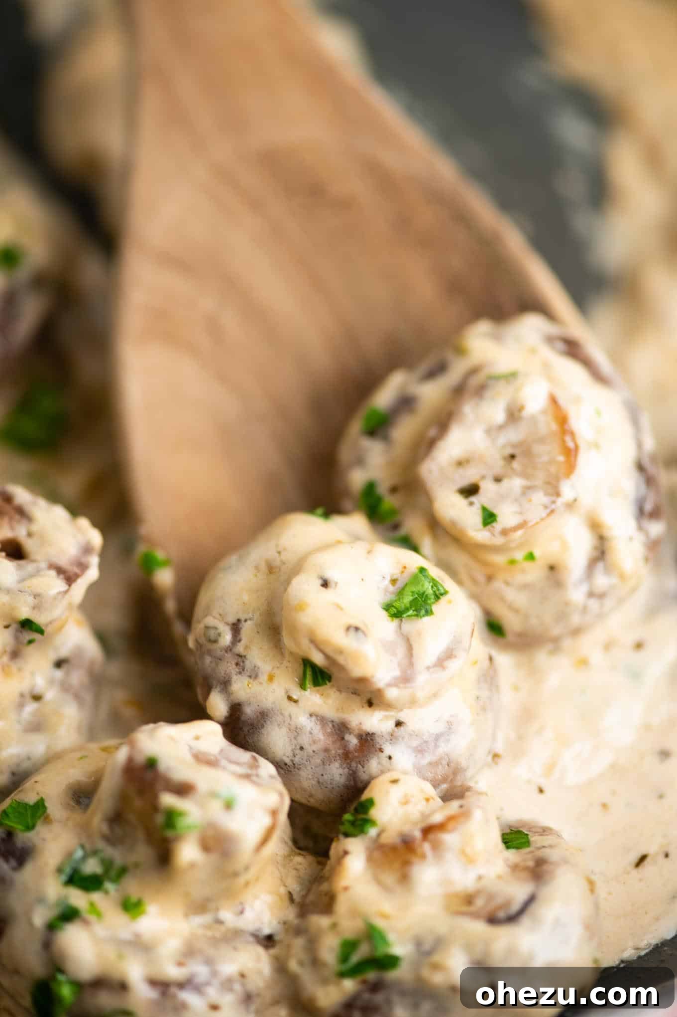 A wooden spoon delicately scooping creamy garlic parmesan mushrooms from a serving dish, highlighting the rich sauce.
