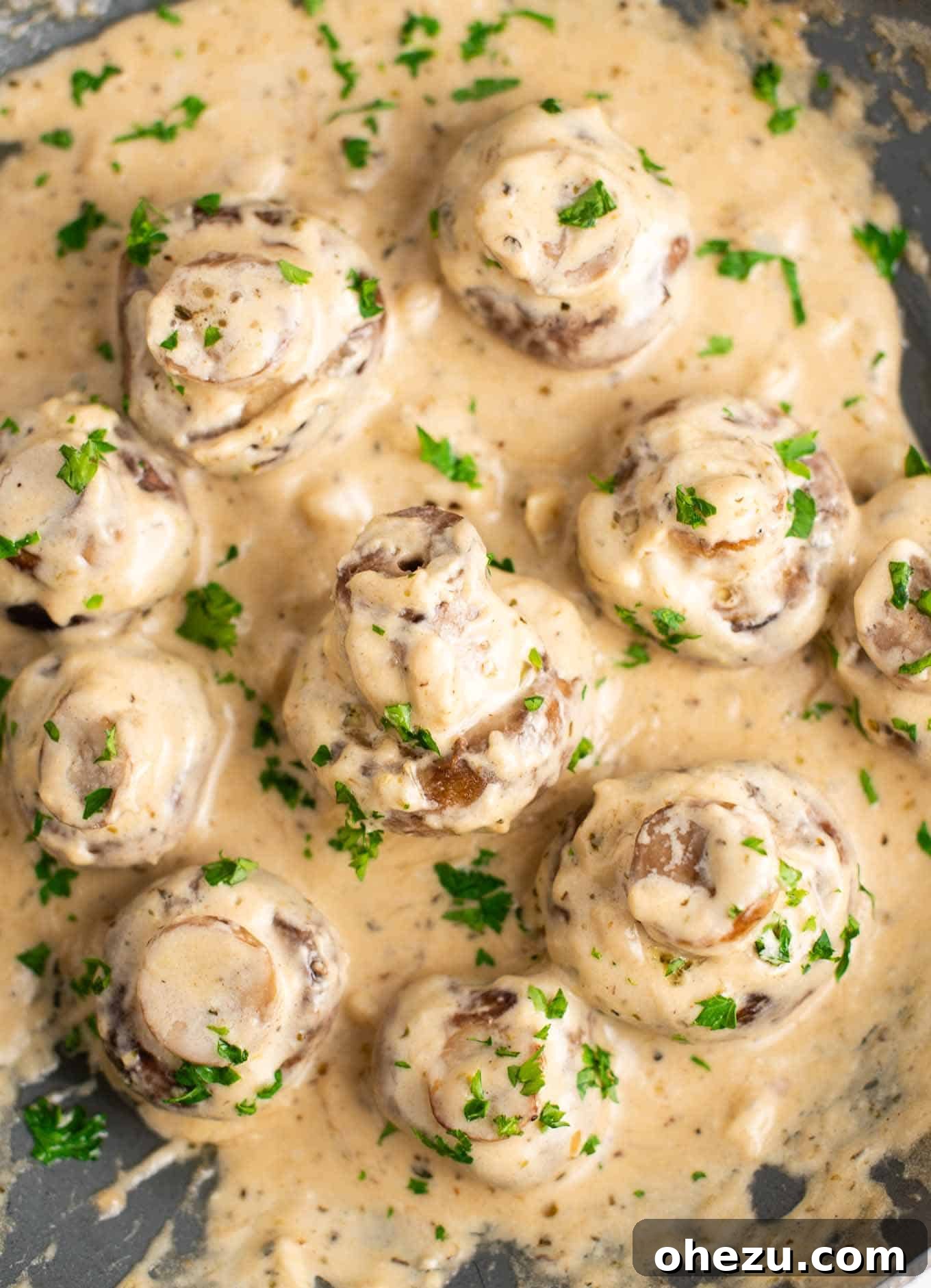 Overhead view of creamy garlic mushrooms bubbling gently in a skillet, adorned with fresh parsley.