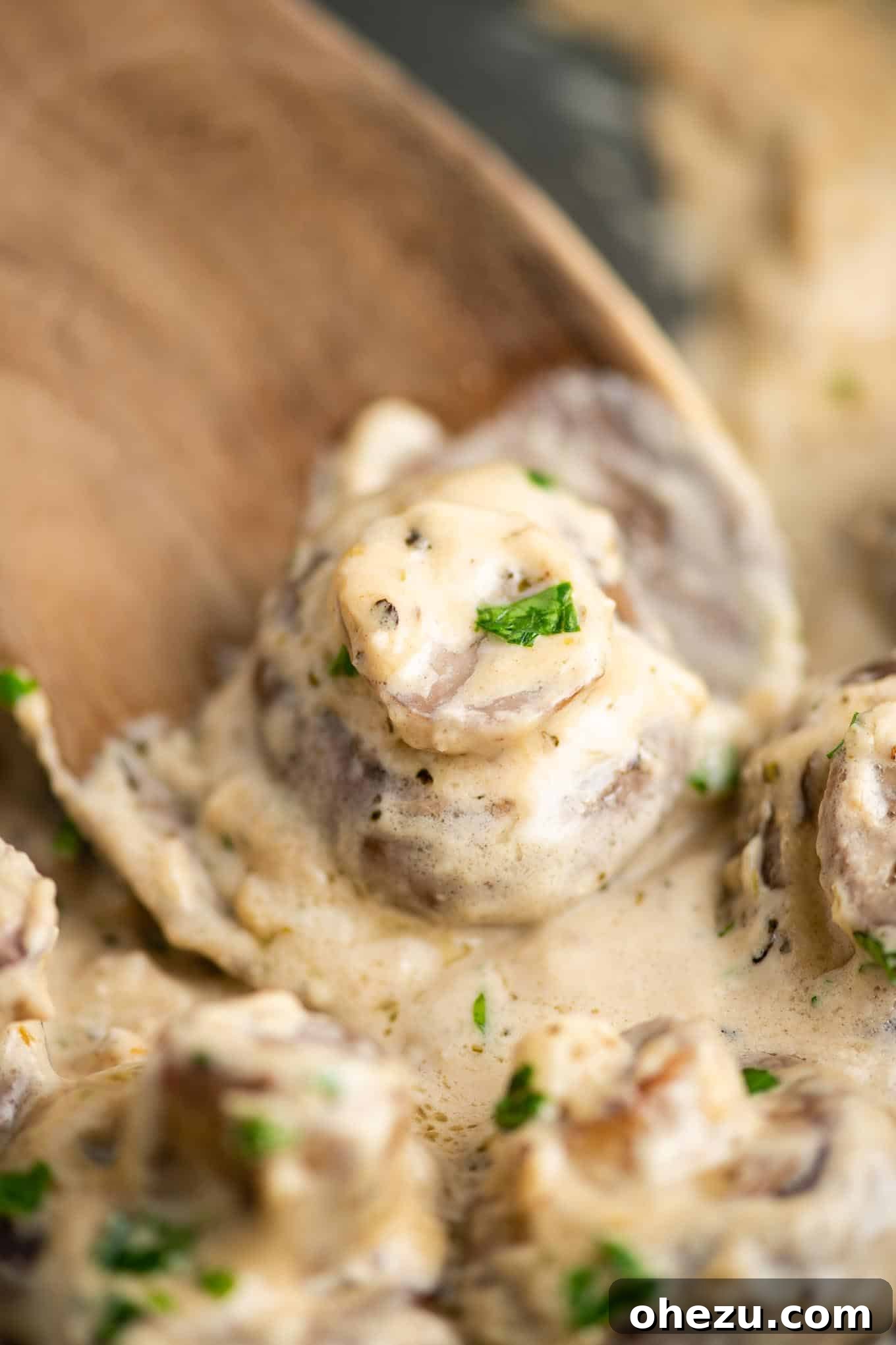 A single creamy garlic mushroom resting on a wooden spoon, perfectly coated in the rich sauce, ready to be enjoyed.