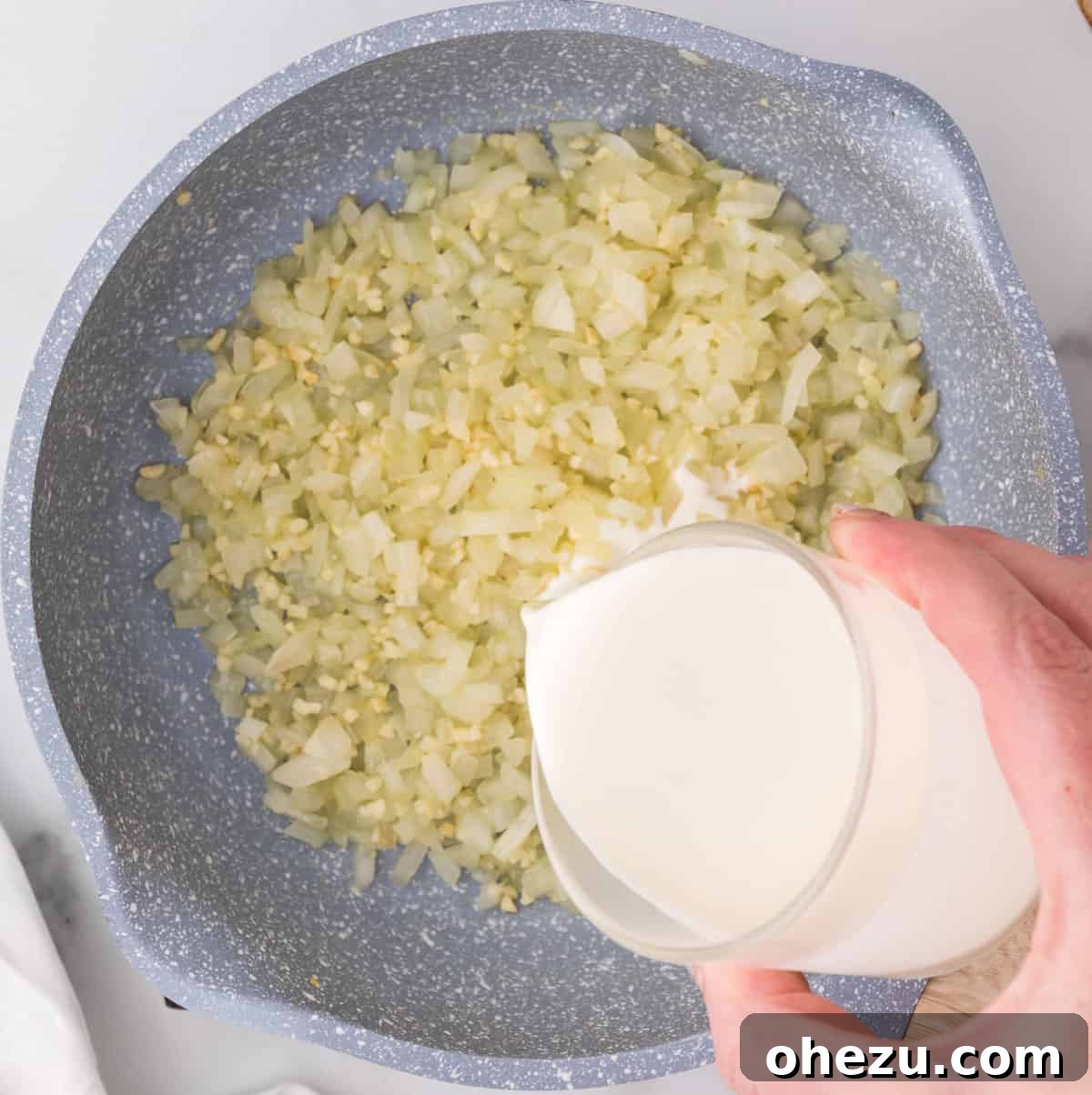 Ultimate Cheesy Brussels Sprouts 7 Heavy cream being poured into a skillet with sautéed garlic and onion, beginning the creamy cheese sauce.