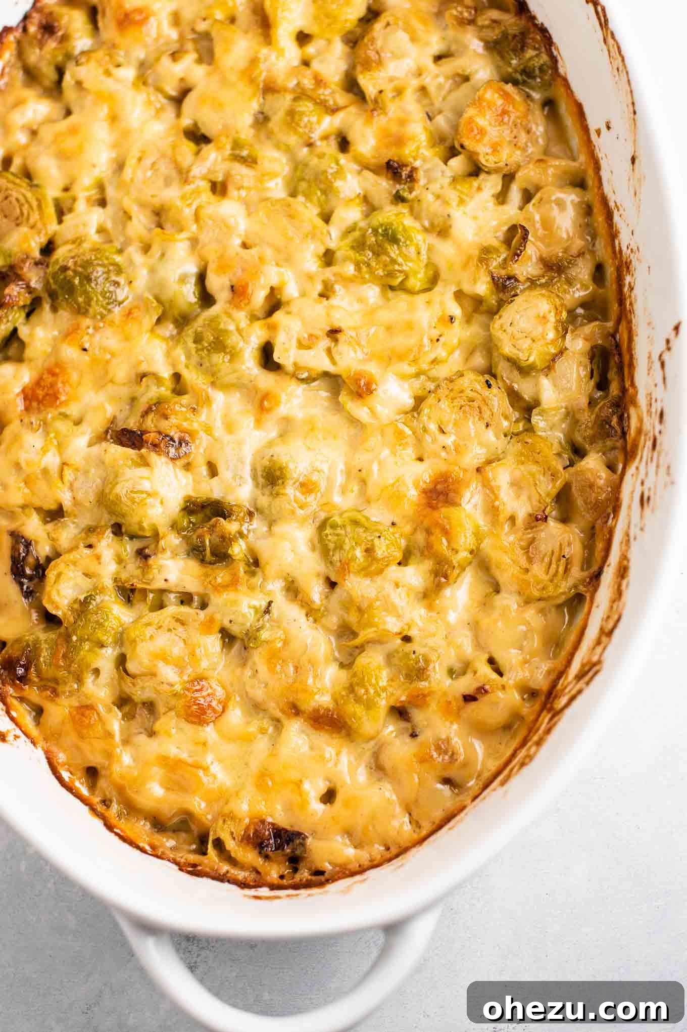 Ultimate Cheesy Brussels Sprouts 9 An overhead shot of a freshly baked cheesy Brussels sprouts gratin, with its golden-brown, bubbling cheese crust, in a white oval dish.