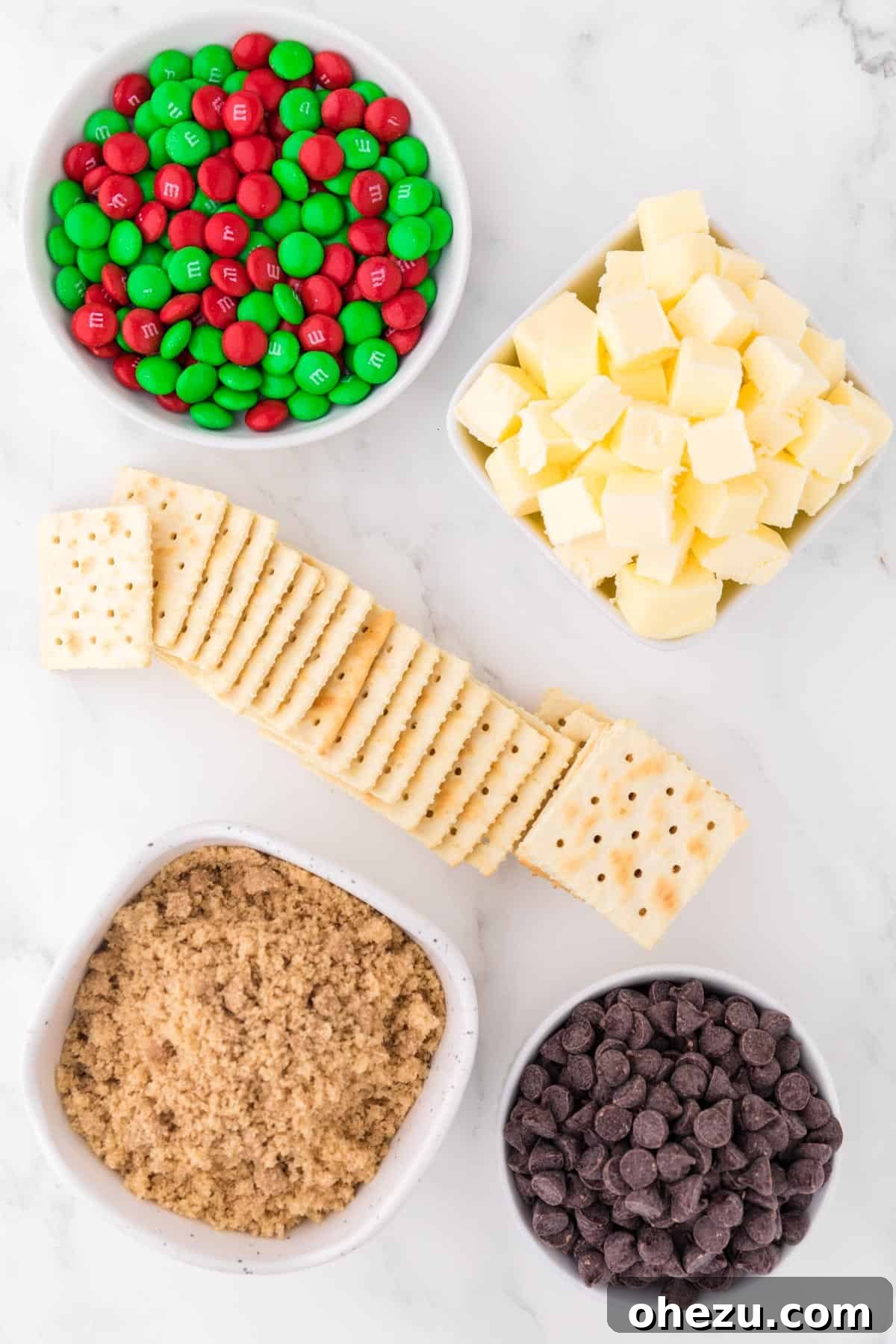 Irresistible Christmas Toffee Bark 5 A flat lay photograph displaying all the simple ingredients required to make delicious saltine toffee candy: saltine crackers, butter, brown sugar, and chocolate chips.