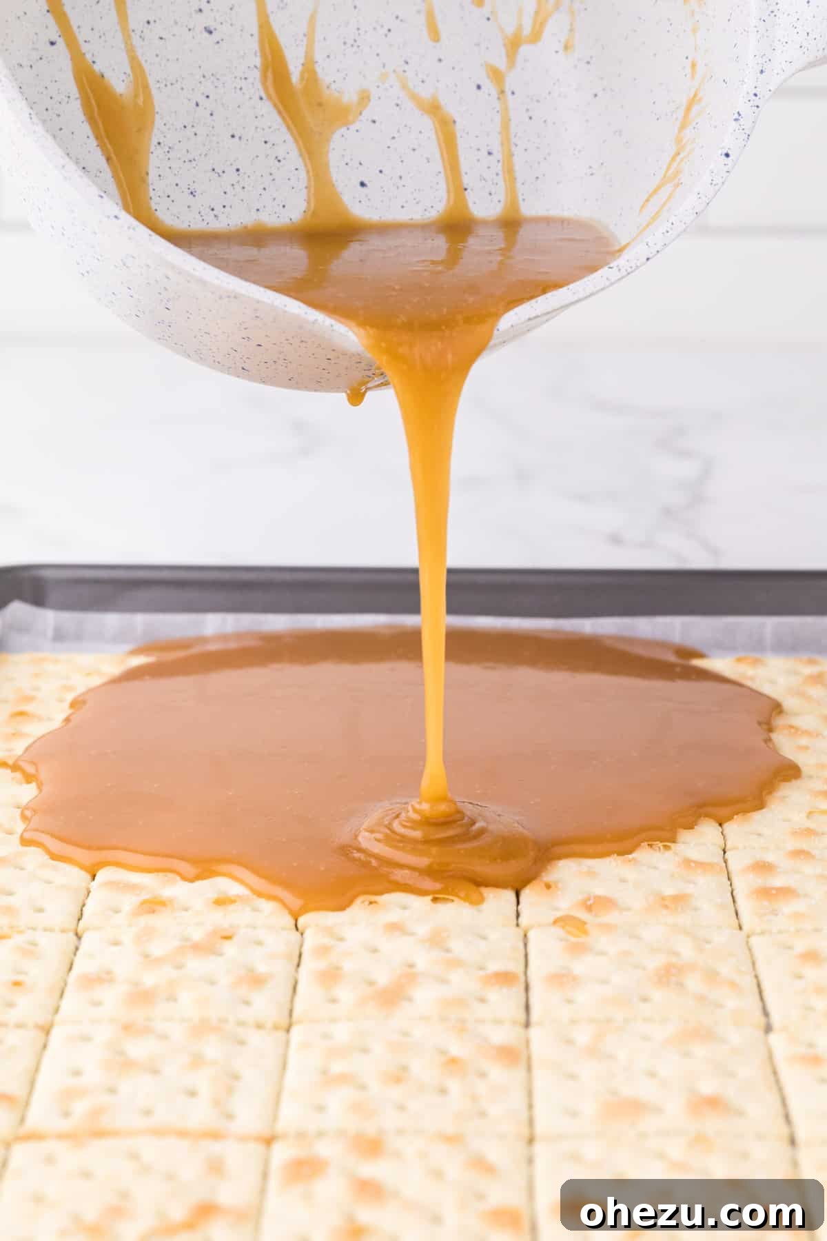 Irresistible Christmas Toffee Bark 9 Thickened toffee mixture being carefully poured and spread over the layer of saltine crackers on the baking sheet.