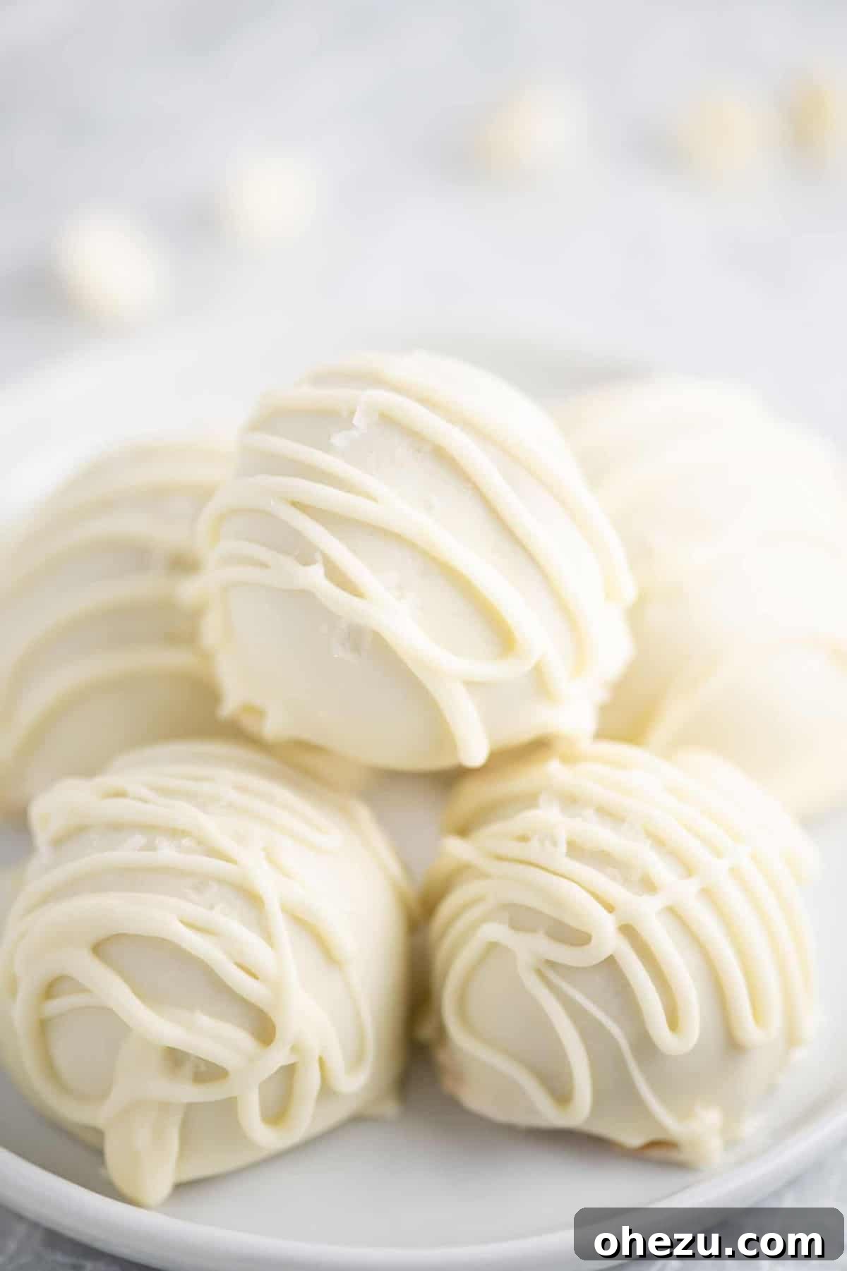 No-Bake White Chocolate Peanut Butter Delights 2 white chocolate peanut butter balls with drizzle stacked on a white plate