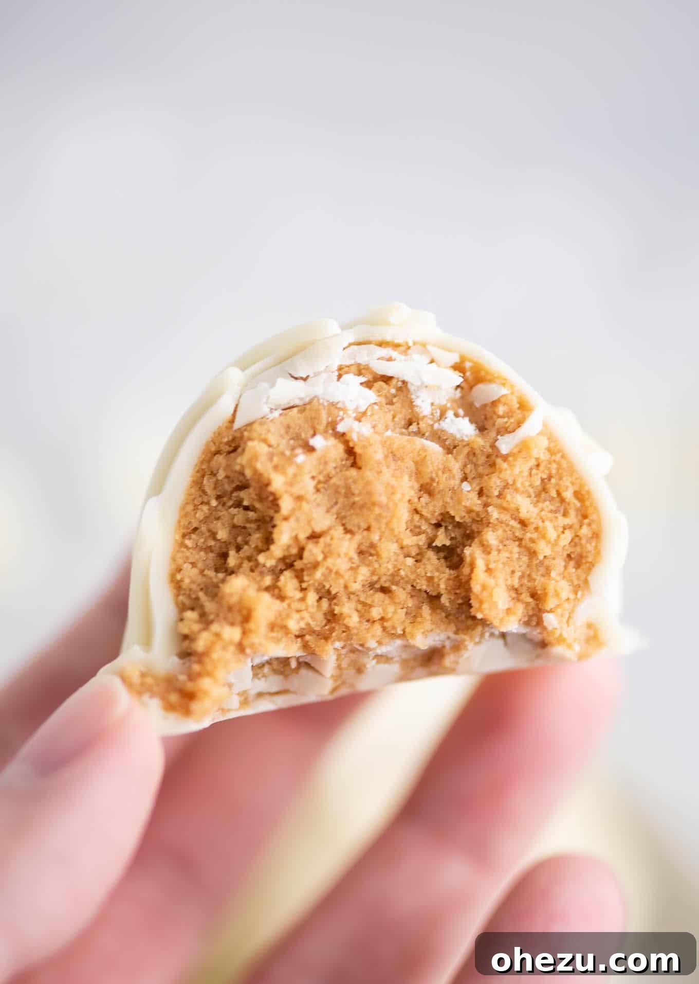 No-Bake White Chocolate Peanut Butter Delights 8 fingers holding a truffle with a bite taken out to show the filling