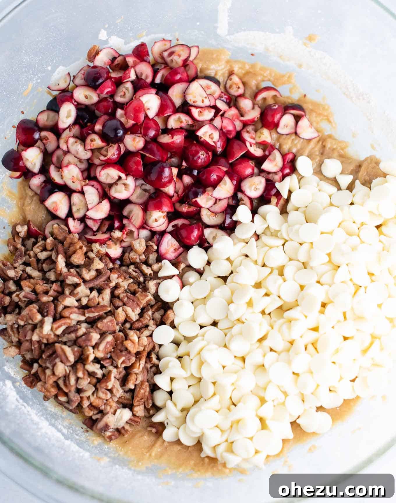 Decadent White Chocolate Cranberry Pecan Cookies 4 Mixing bowl with cookie batter, topped with vibrant chopped cranberries, crunchy pecans, and creamy white chocolate baking chips, ready to be folded in