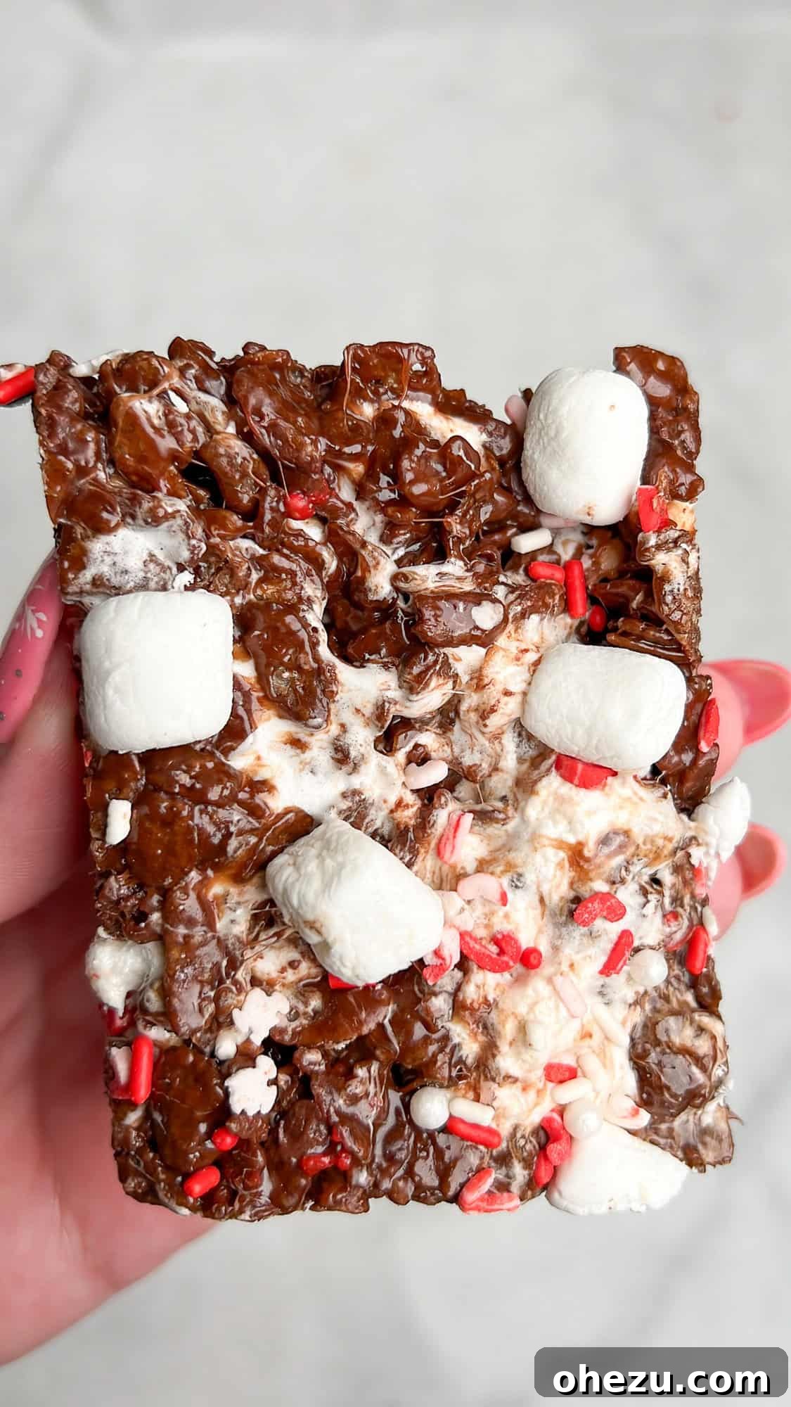 Cozy Cocoa Crisps 15 A hand holding a square of Hot Cocoa Rice Krispie Treat, showcasing its tempting texture and toppings.