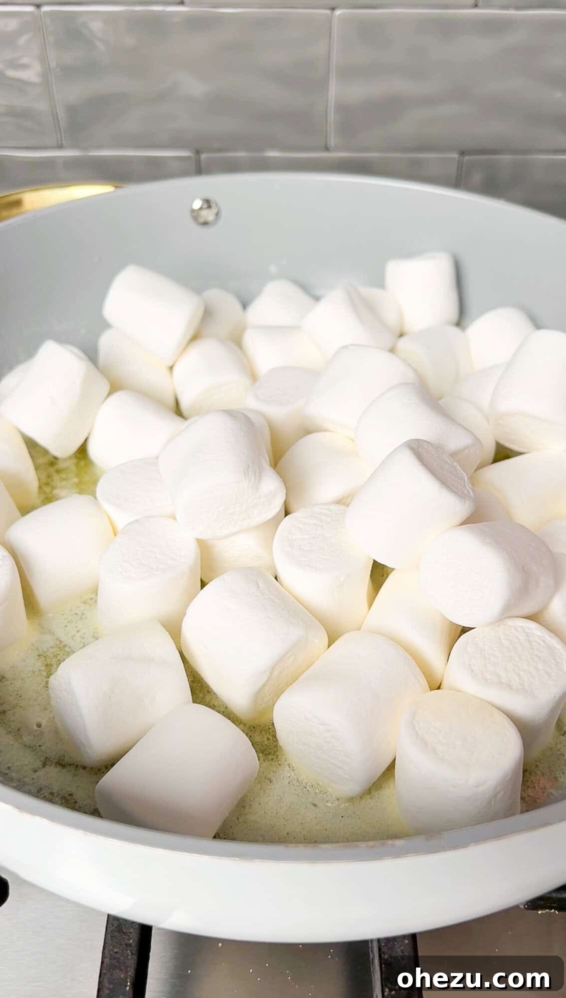 Cozy Cocoa Crisps 6 Mini marshmallows gently melting into a pool of golden butter in a large nonstick pan, creating a smooth, gooey base.