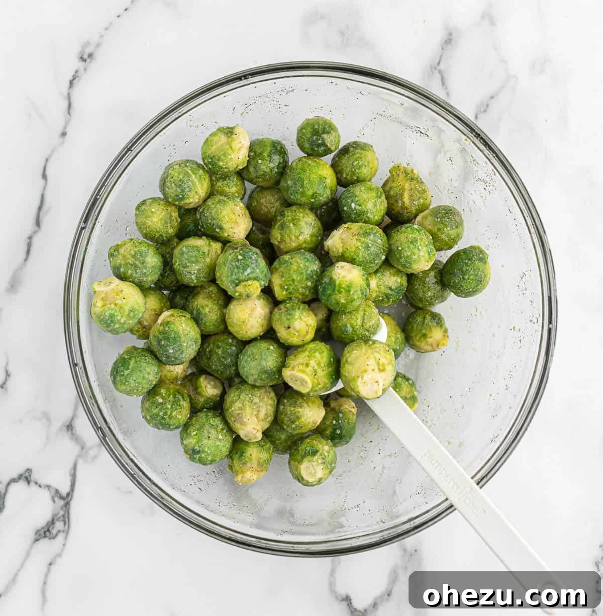 Frozen Brussels sprouts in a large mixing bowl, tossed with olive oil and spices, ready for roasting.