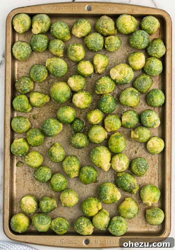 Partially roasted frozen Brussels sprouts on a baking dish, still whole but softened, ready to be cut in half.