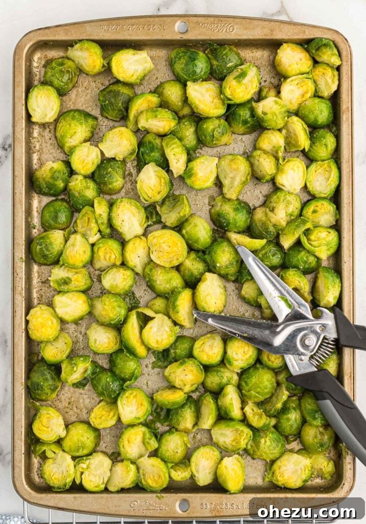 Close-up of frozen Brussels sprouts being efficiently cut in half using kitchen scissors directly on the baking sheet.