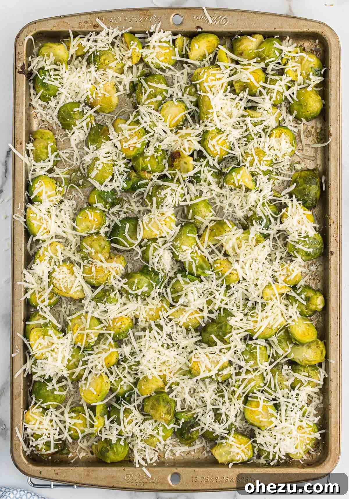 Roasted Brussels sprouts on a baking sheet, freshly topped with a generous layer of grated Parmesan cheese before the final roast.