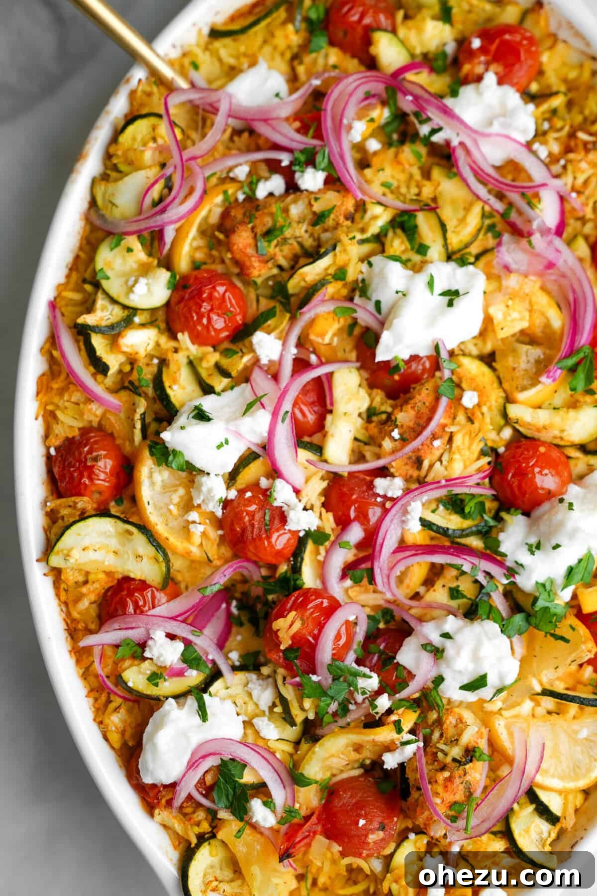 Zesty Greek Chicken Casserole 2 Large casserole dish filled with golden chicken tzatziki, ready to serve, with a gold spoon resting inside.