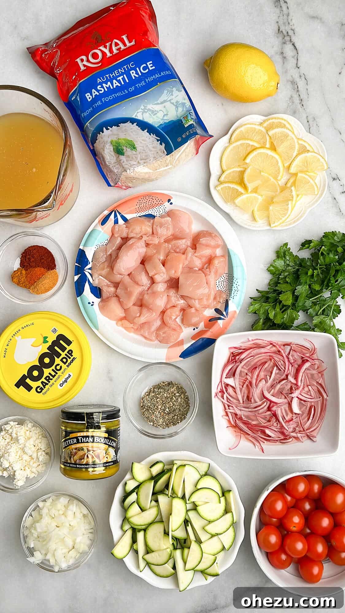 Zesty Greek Chicken Casserole 4 Arrangement of fresh ingredients for chicken tzatziki casserole, including diced chicken, zucchini, tomatoes, rice, and seasoning spices, all measured out on a counter.