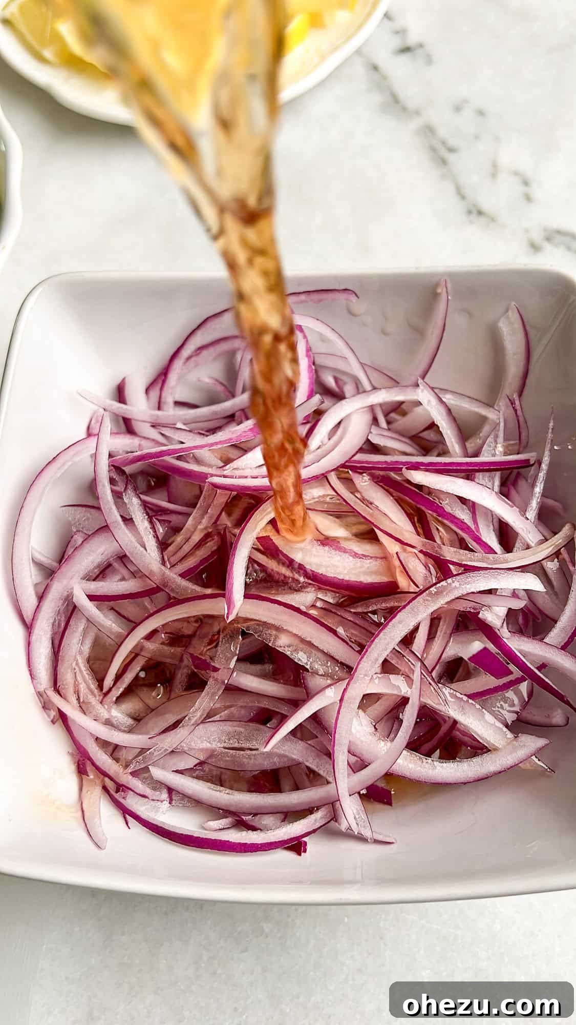 Zesty Greek Chicken Casserole 6 Thinly sliced red onions submerged in a pickling liquid in a glass bowl.