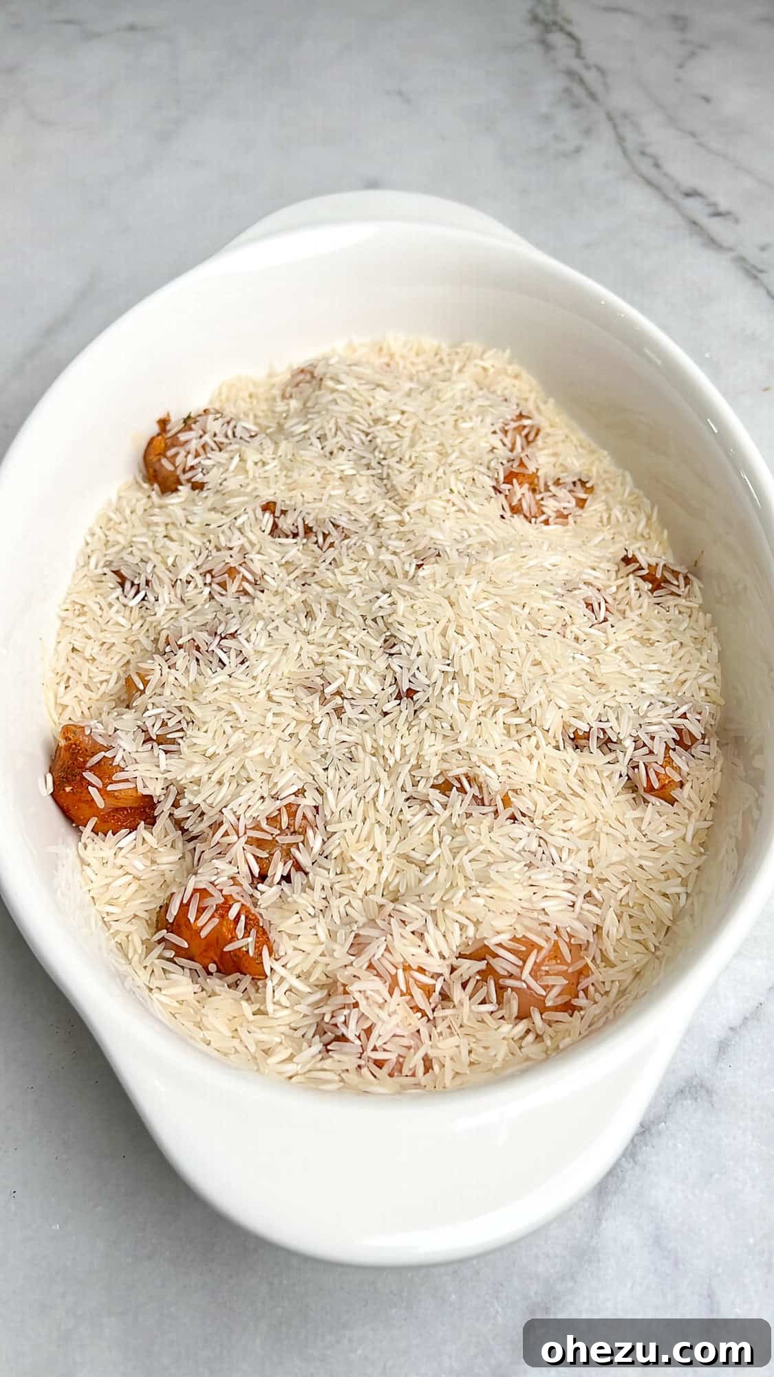 Zesty Greek Chicken Casserole 8 Uncooked basmati rice evenly spread over the seasoned chicken in a casserole dish.