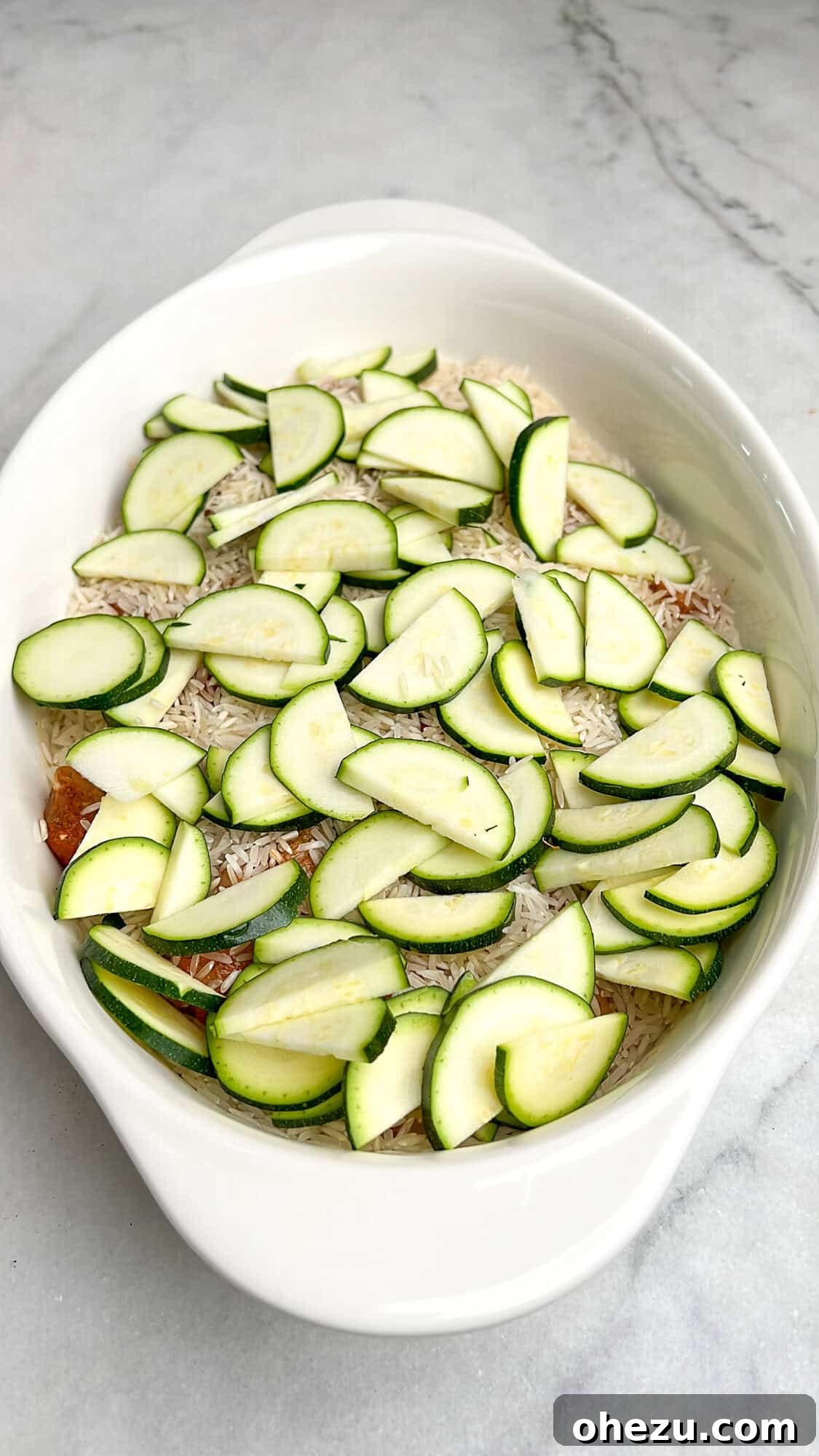 Zesty Greek Chicken Casserole 9 Sliced zucchini and whole grape tomatoes arranged over the rice and chicken in the casserole dish.