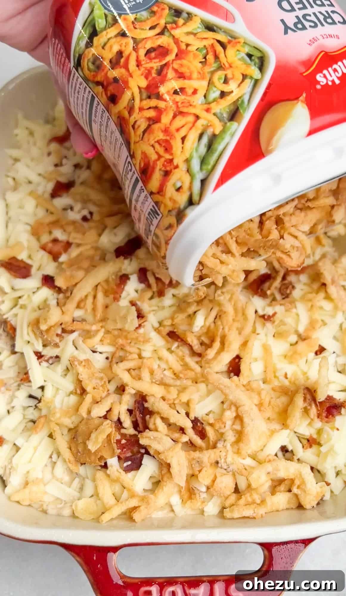 Pouring French fried onions over the dip in a pan before baking