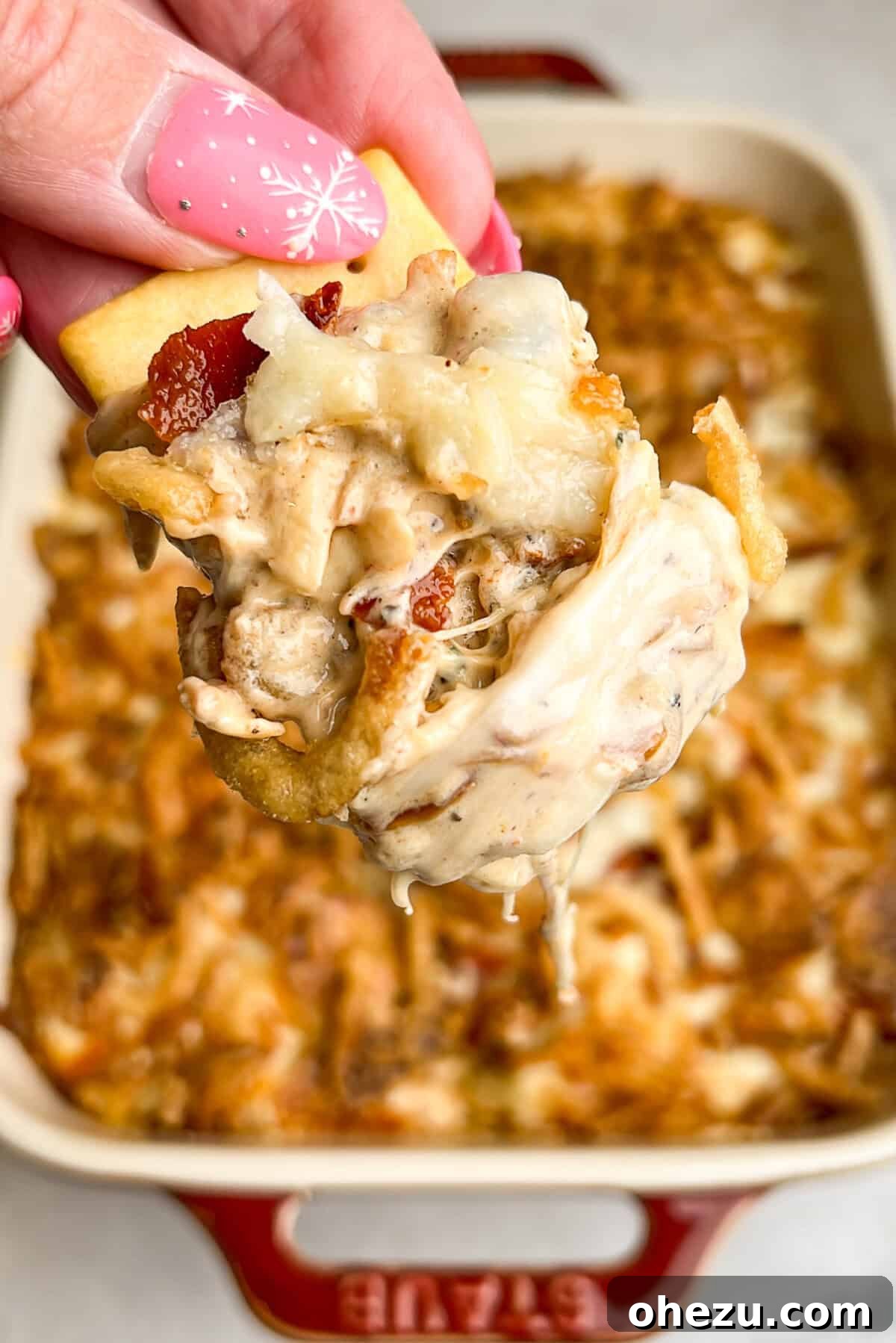 Hot caramelized onion dip with bacon served on a cracker, showing melted cheese