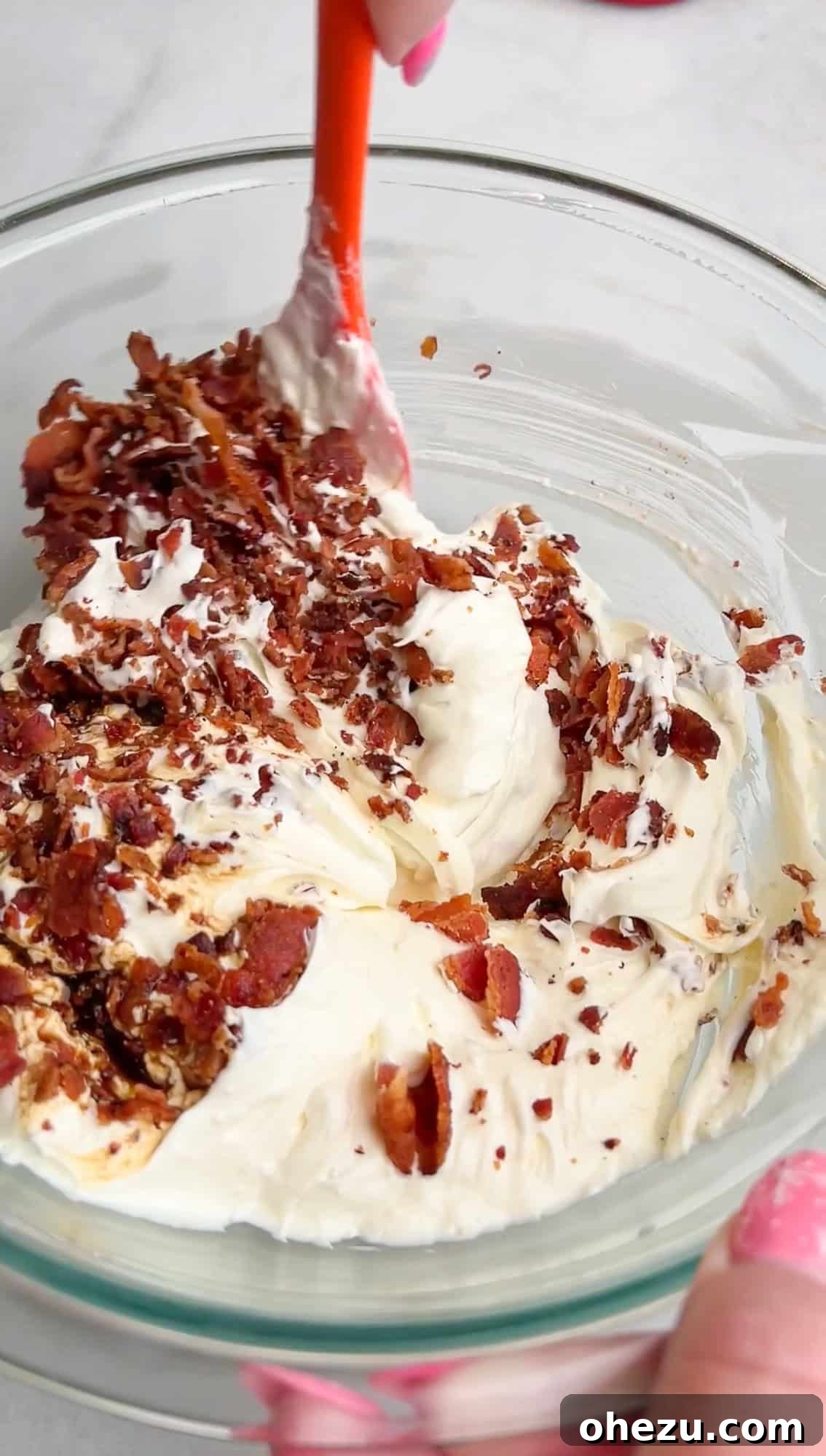Adding diced bacon and shredded cheese to the creamy onion dip base