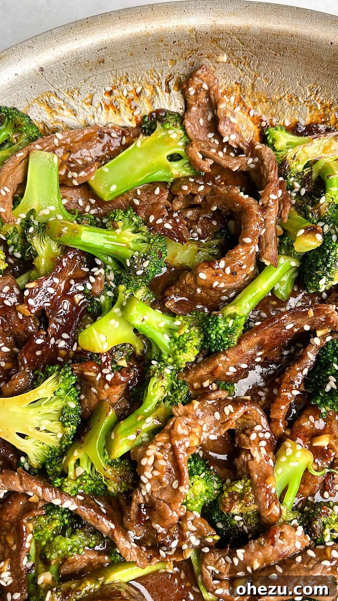 Close-up of beef and broccoli simmering in a pan, glossy with sauce