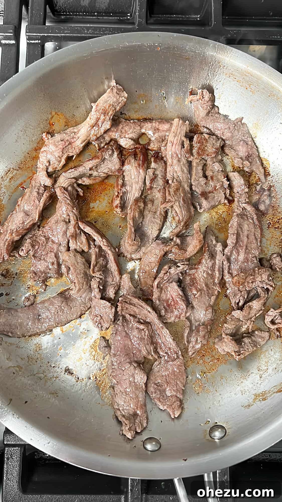 Thin strips of flank steak searing in a hot skillet