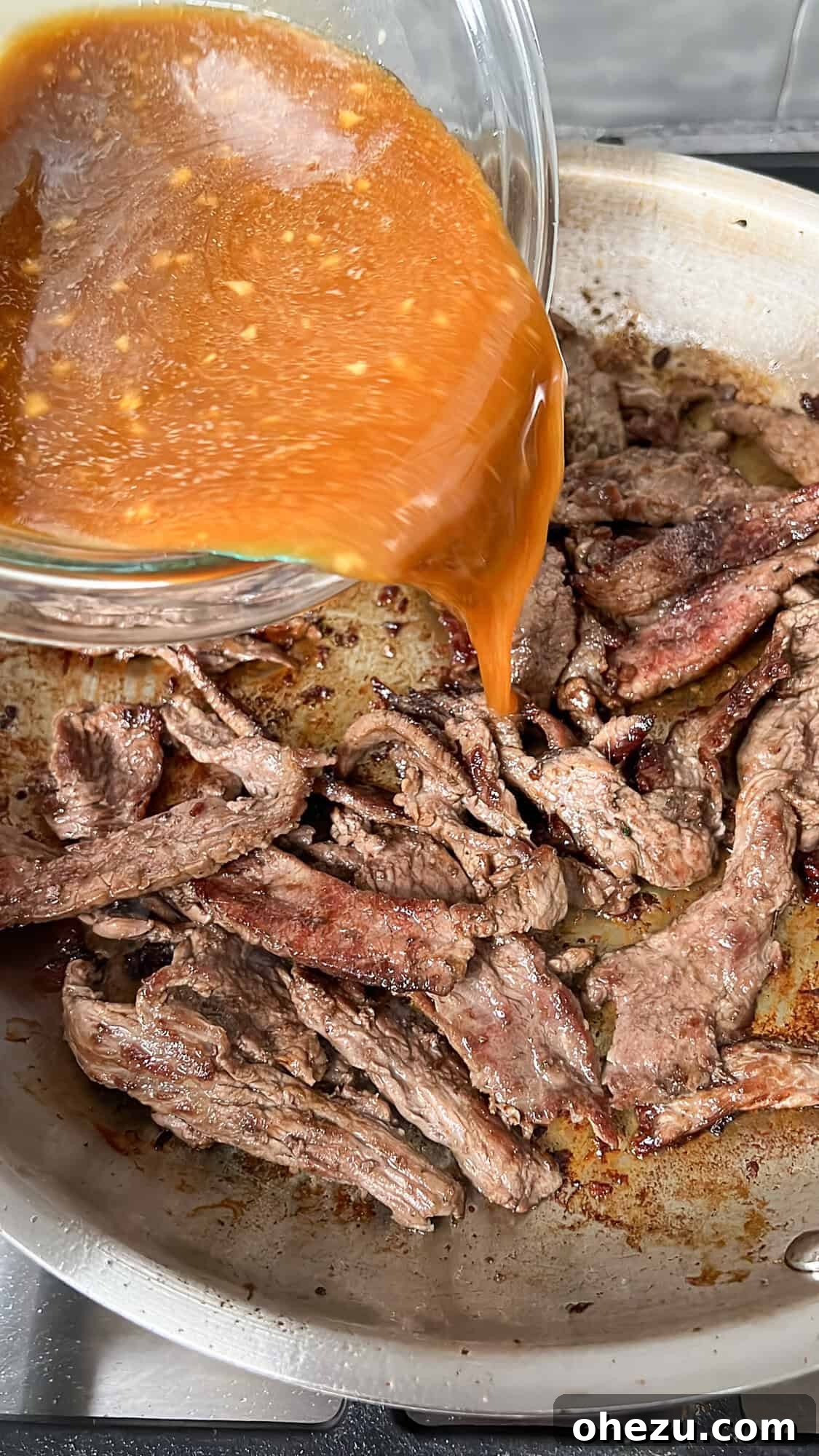 Savory sauce being poured over seared beef in a pan