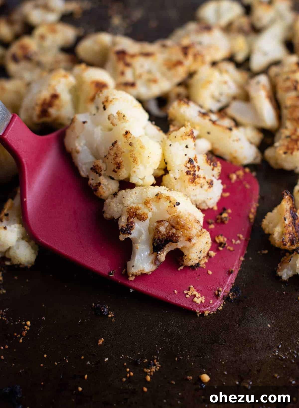 Golden-brown roasted frozen cauliflower florets on a baking sheet, ready to be served with a red spatula.