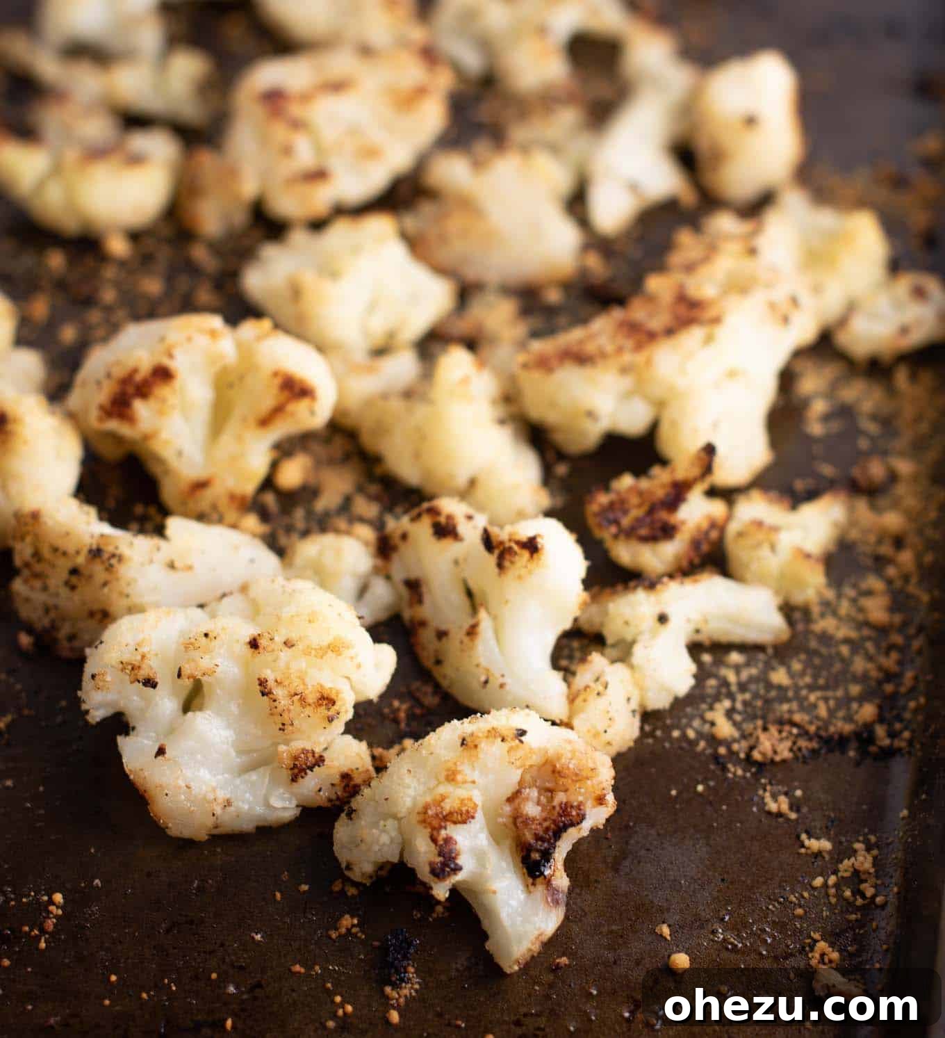 Close-up of perfectly roasted cauliflower florets with golden-brown edges on a baking sheet.