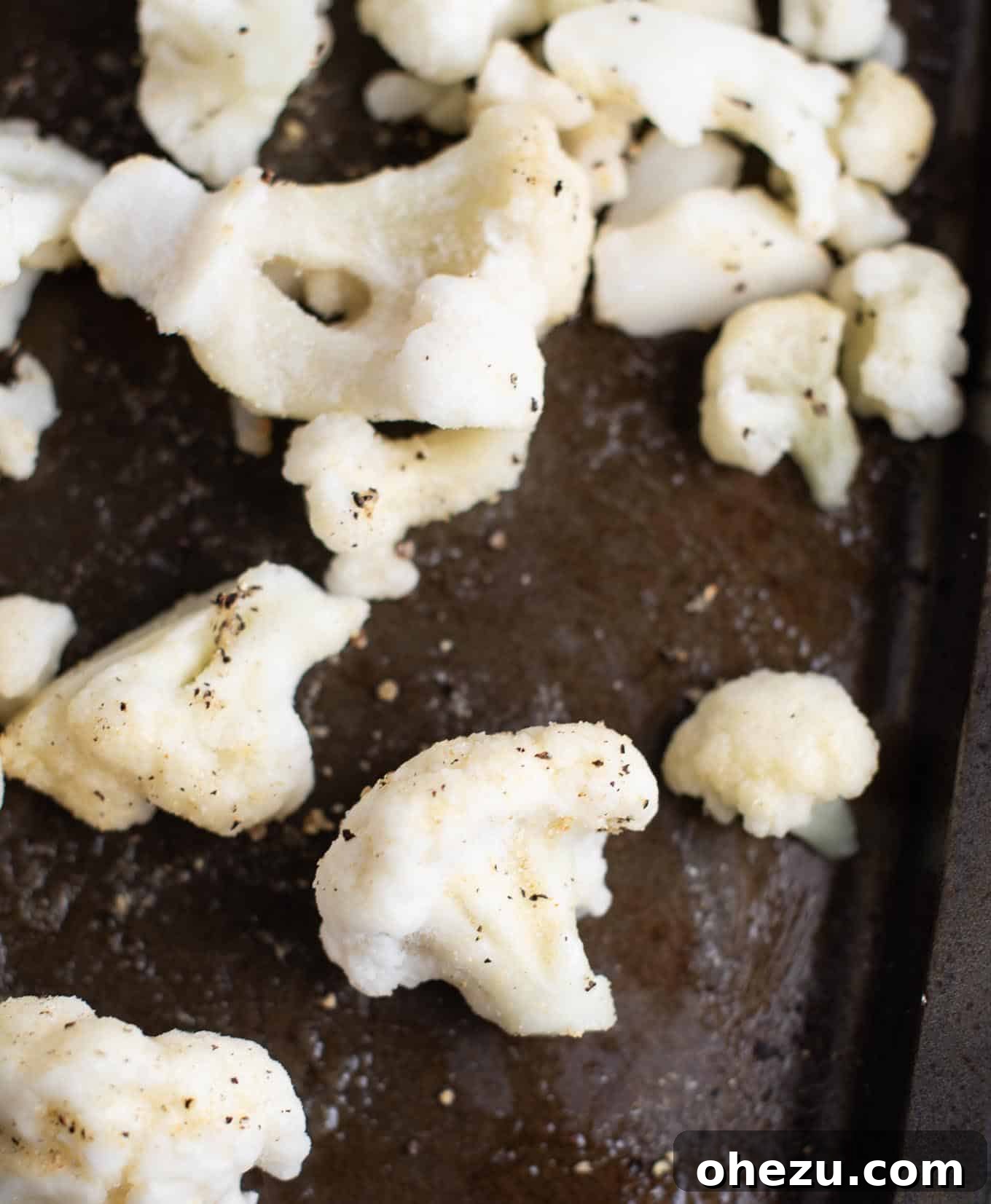 Frozen cauliflower florets arranged on a baking sheet, lightly sprinkled with spices before roasting.