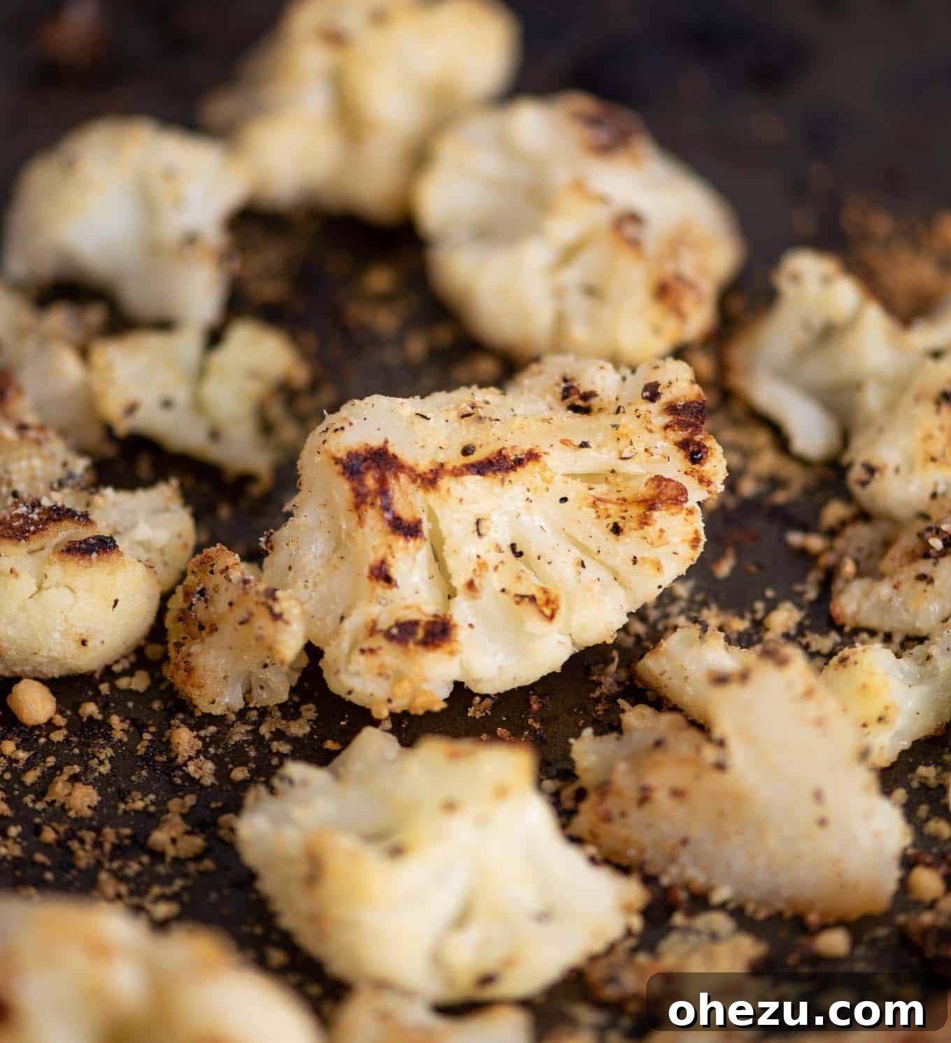 Detailed view of perfectly roasted cauliflower on a baking sheet, showing crispy texture and browned edges.