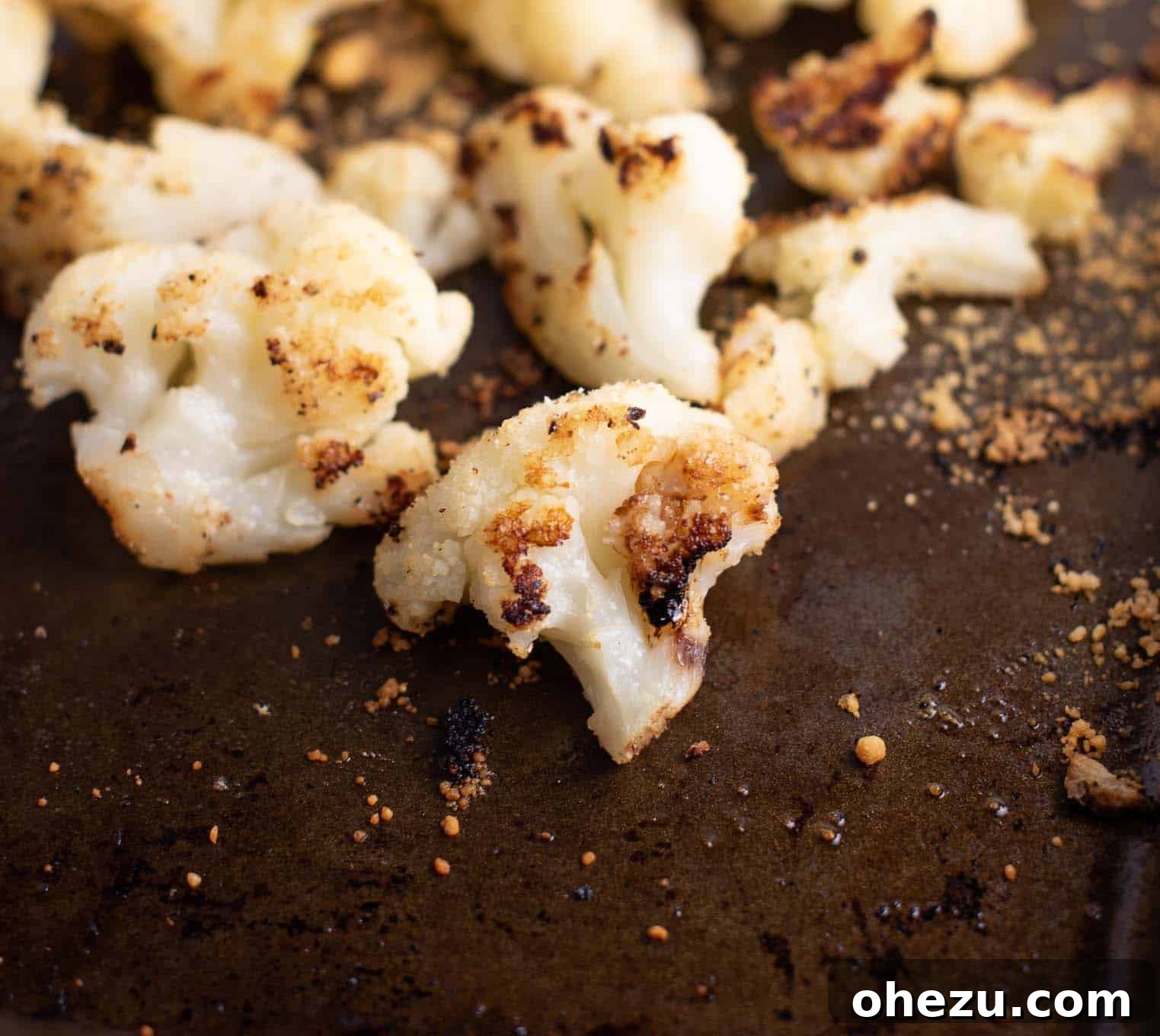 Roasted frozen cauliflower with melted parmesan cheese on a brown baking sheet, ready to serve.