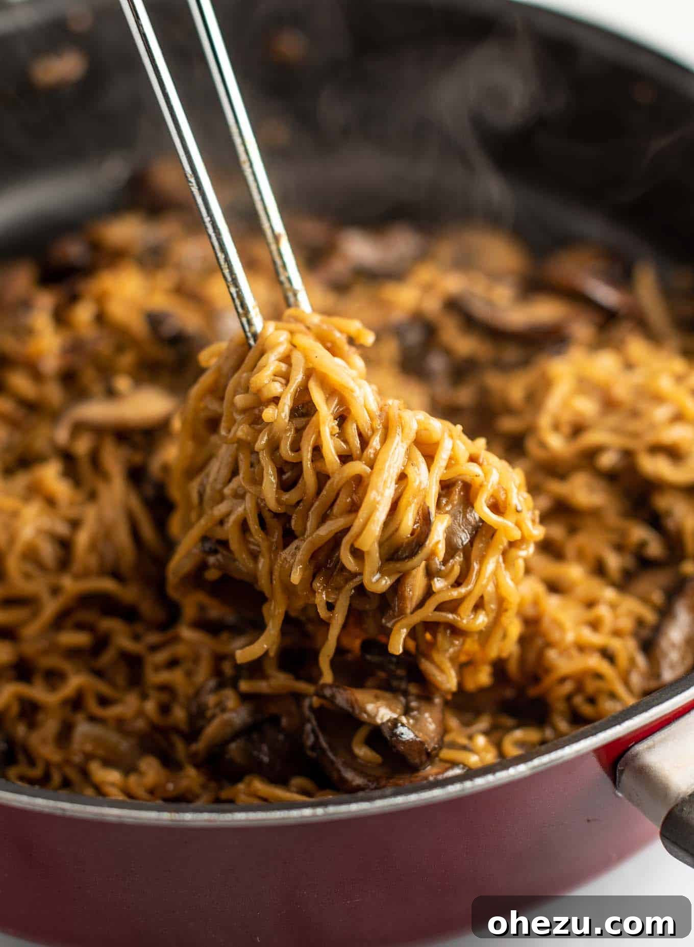 tongs pulling ramen noodles from a pan, showing saucy, perfectly cooked mushroom ramen