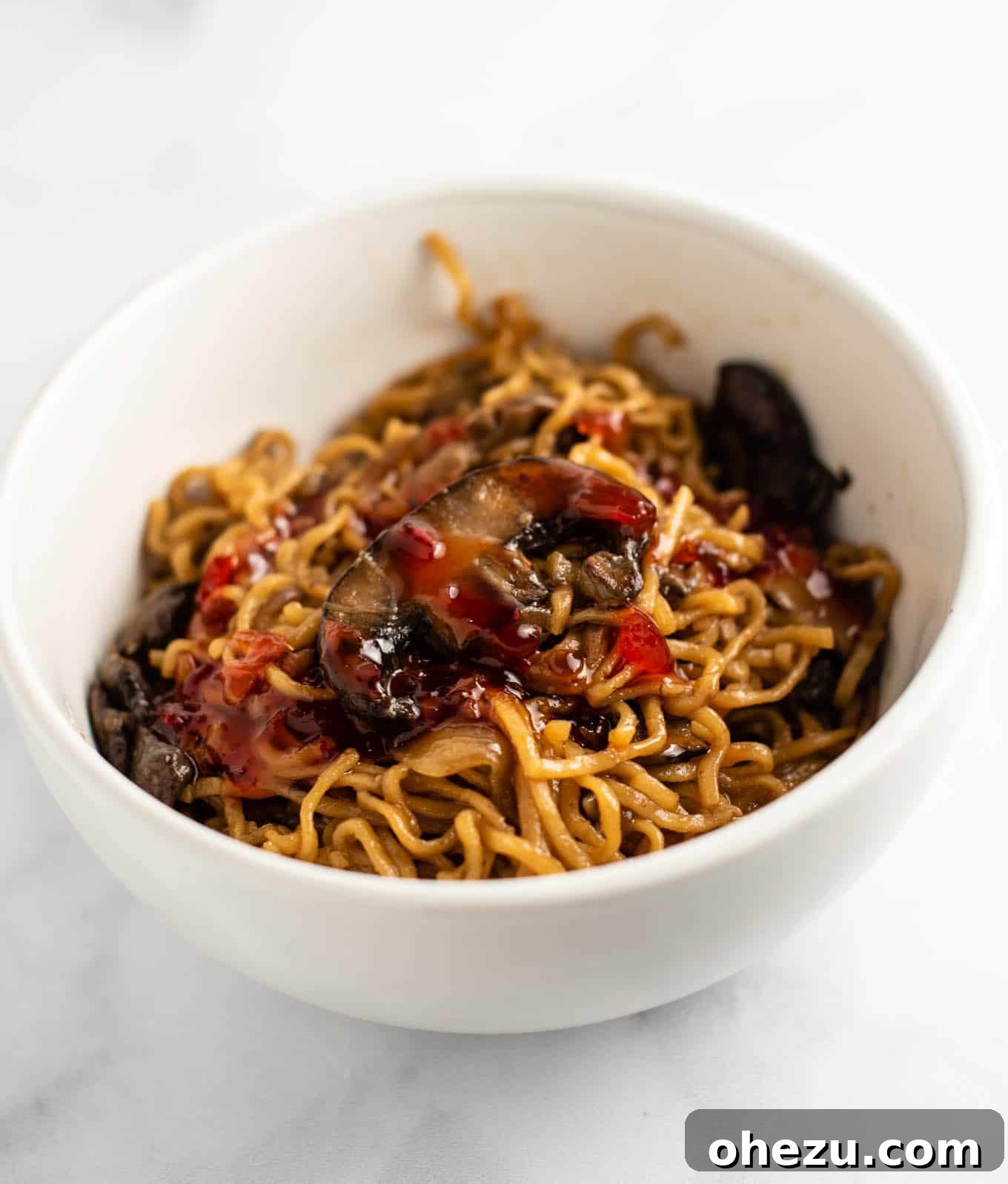 mushroom noodles with sweet chili sauce on top in a white bowl, ready to eat