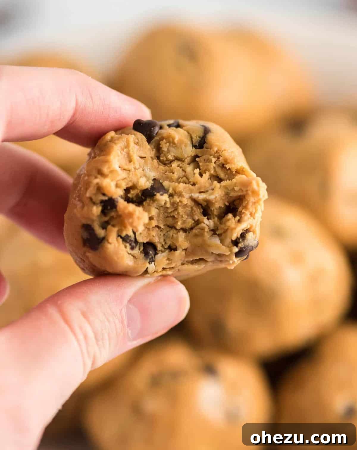 Close-up of fingers holding a freshly made no bake energy ball with a bite taken out, showing the oats and chocolate chips inside.