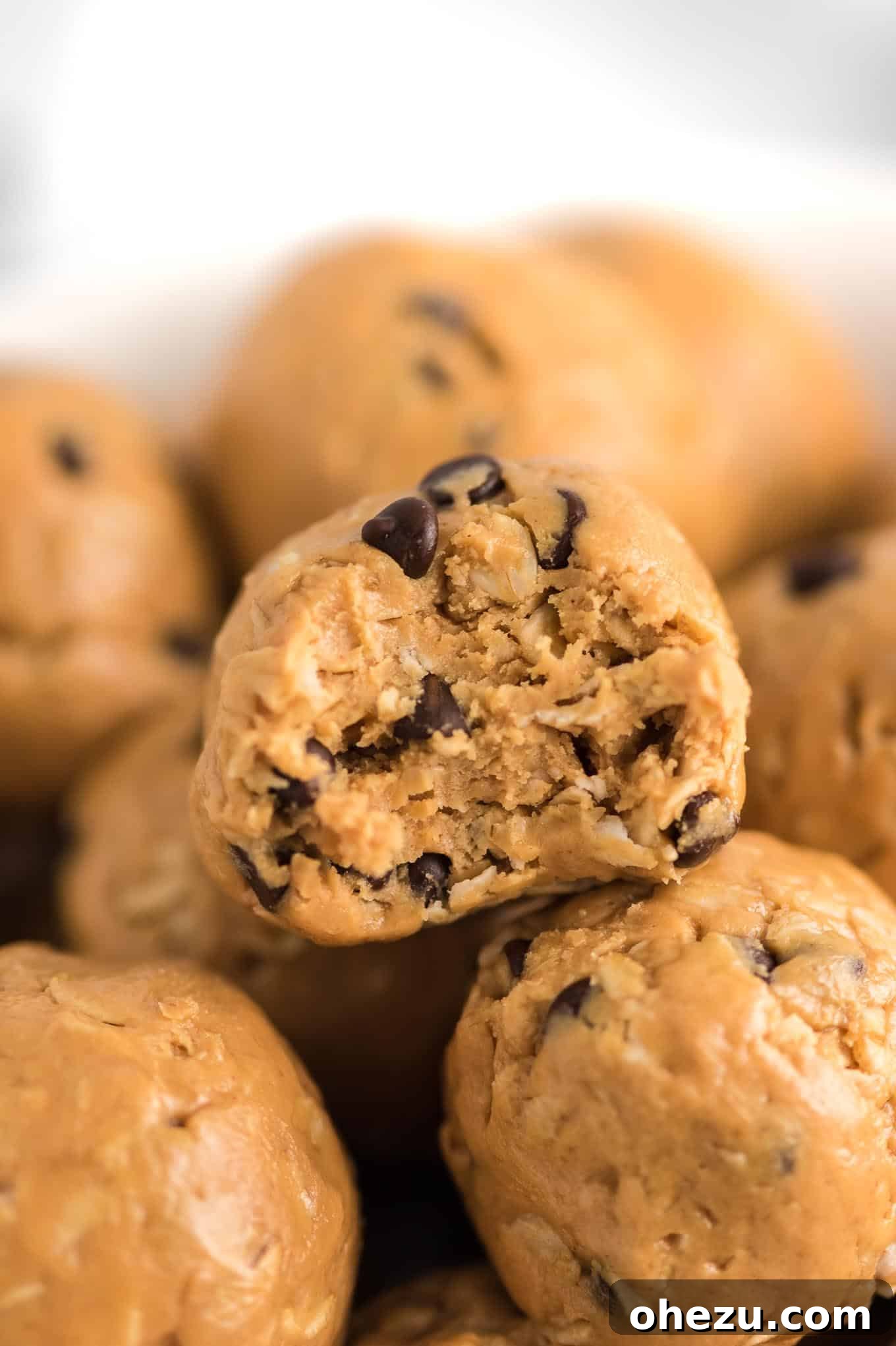 A perfectly shaped energy ball with a bite taken out, sitting atop a small stack of other energy balls, showcasing its delicious interior.