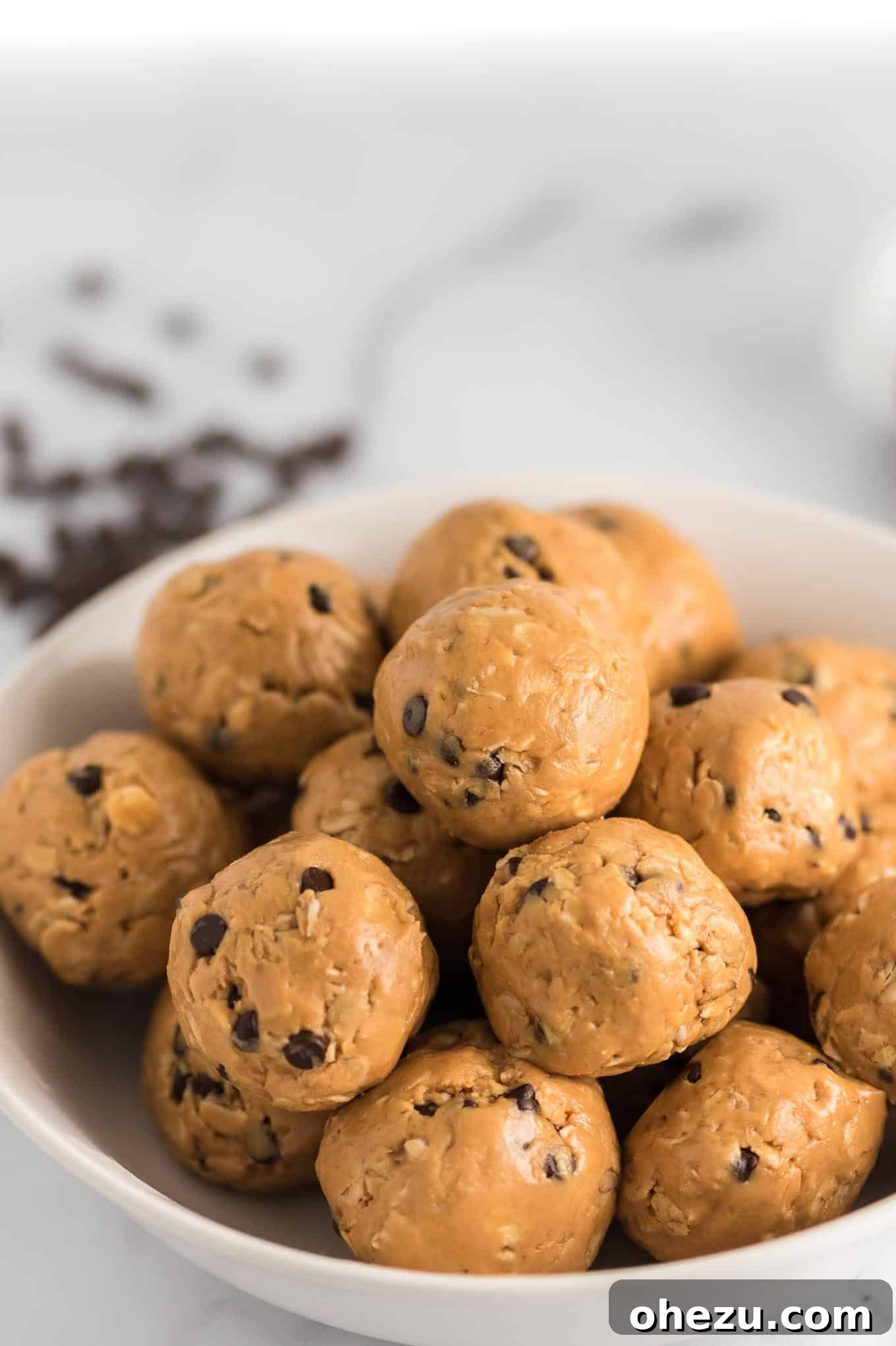 A bowl filled with numerous no bake energy balls, some visible chocolate chips, set against a blurred background.