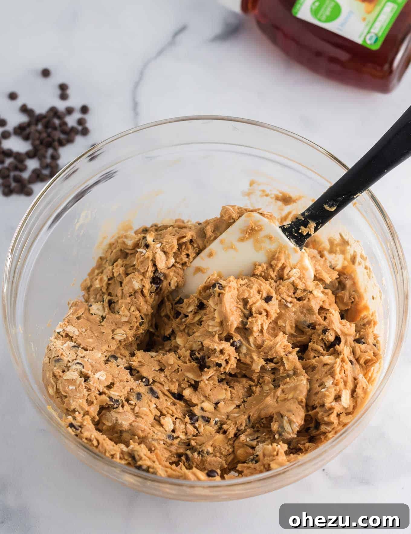 The energy ball ingredients are fully mixed together in a bowl using a rubber spatula, showing a thick, cohesive dough.