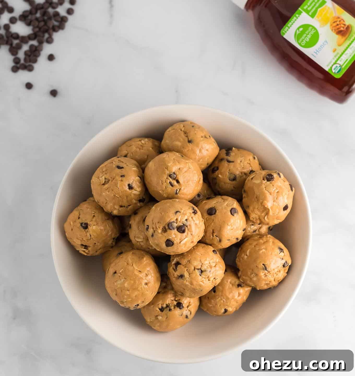 A stack of firm no bake energy balls, with a drizzle of honey and scattered chocolate chips visible in the background.
