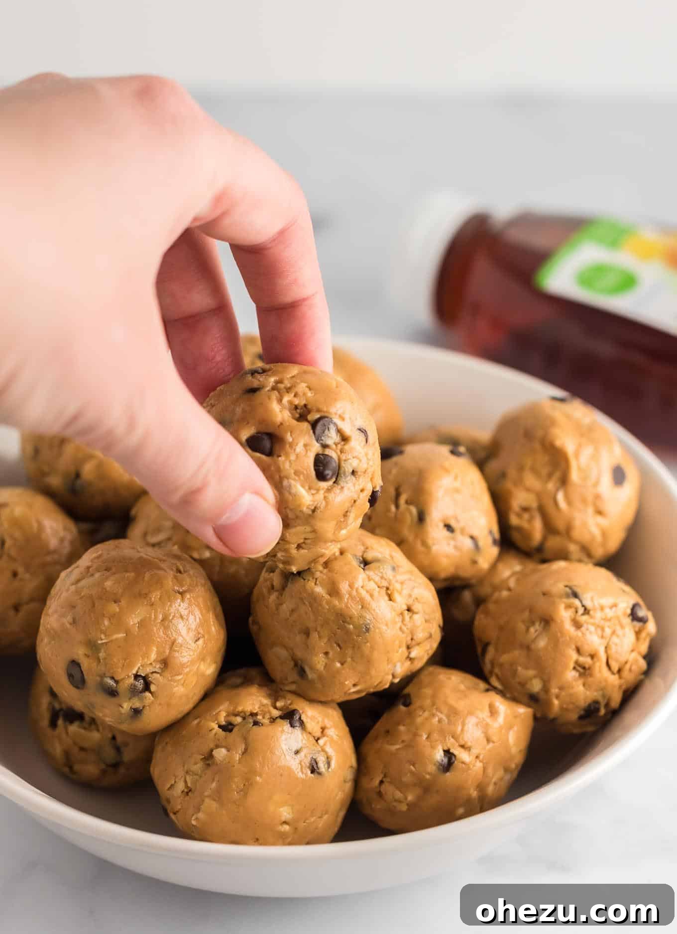 Fingers reaching into a stacked bowl of energy balls to pick one up, highlighting their ready-to-eat appeal.